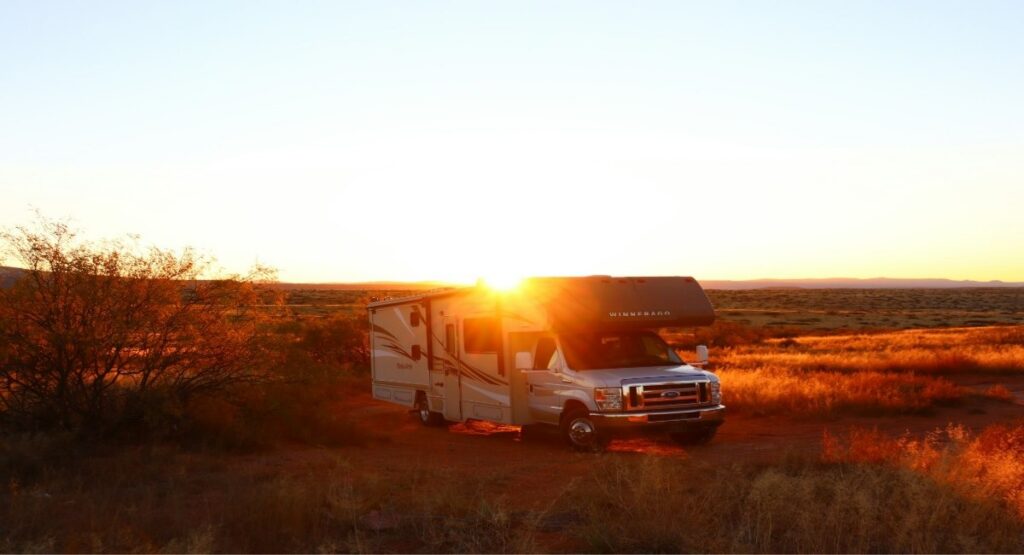 A Winnebago Class C motorhome parked on an open desert plain at golden hour sunset near Sedona, Arizona
