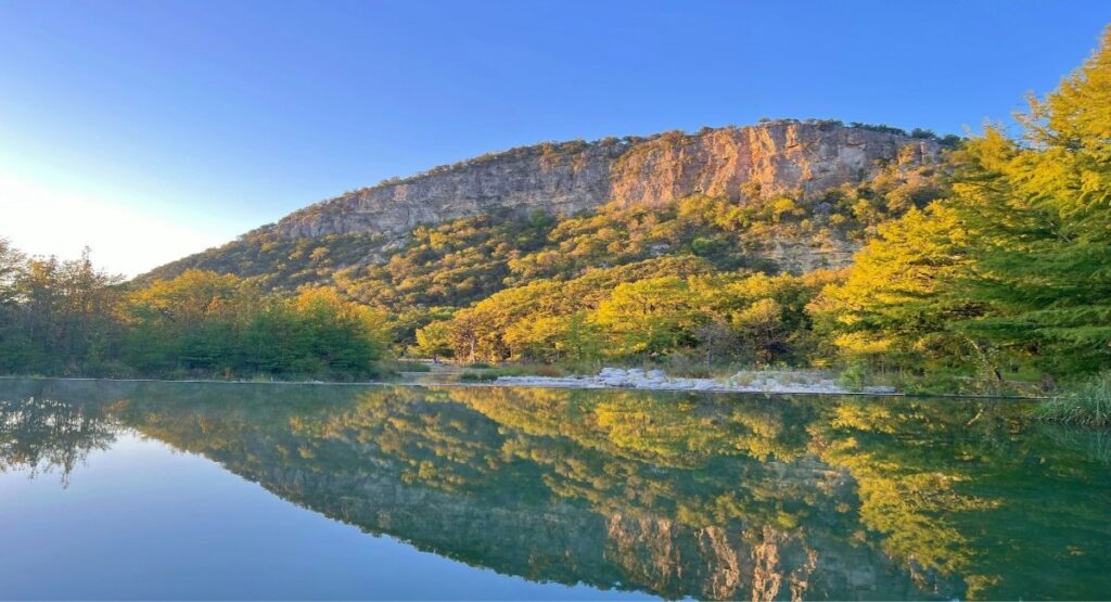 Golden fall foliage and limestone cliffs reflect in the glassy waters of the Frio River at Garner State Park