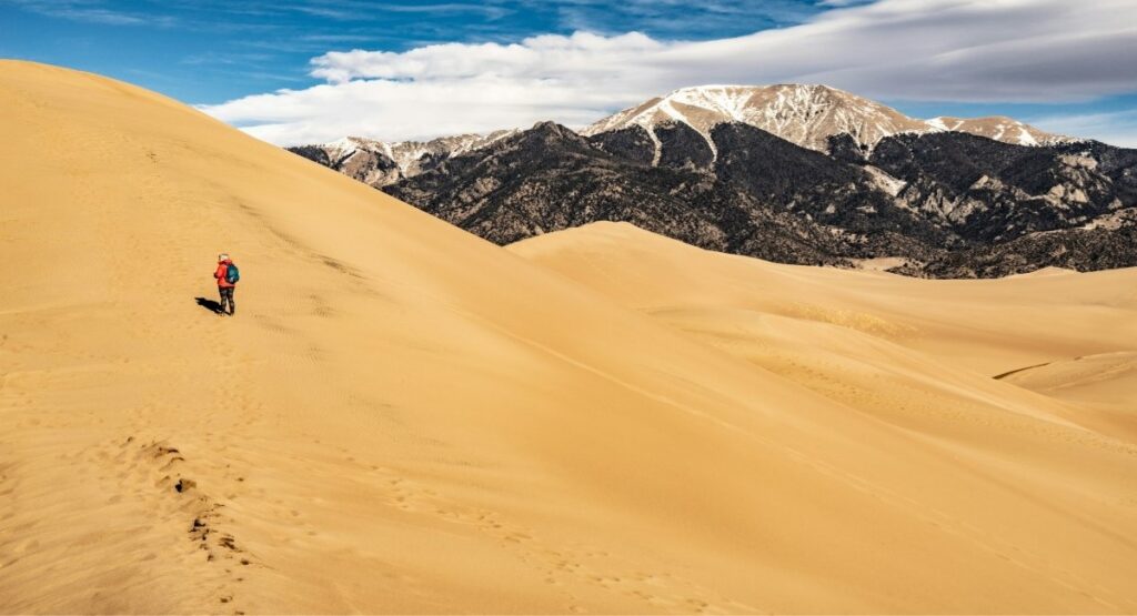 A hiker in a red jacket climbing the vast golden sand dunes at Great Sand Dunes National Park, Colorado