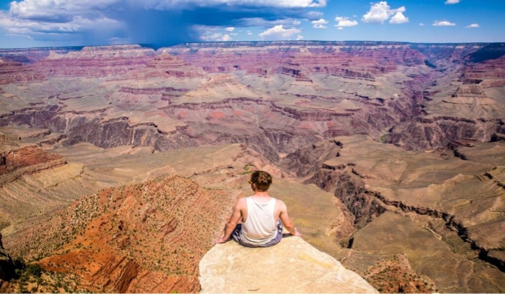 A man sits on a rock ledge at the South Rim, taking in the sweeping layered canyon views at Grand Canyon National Park