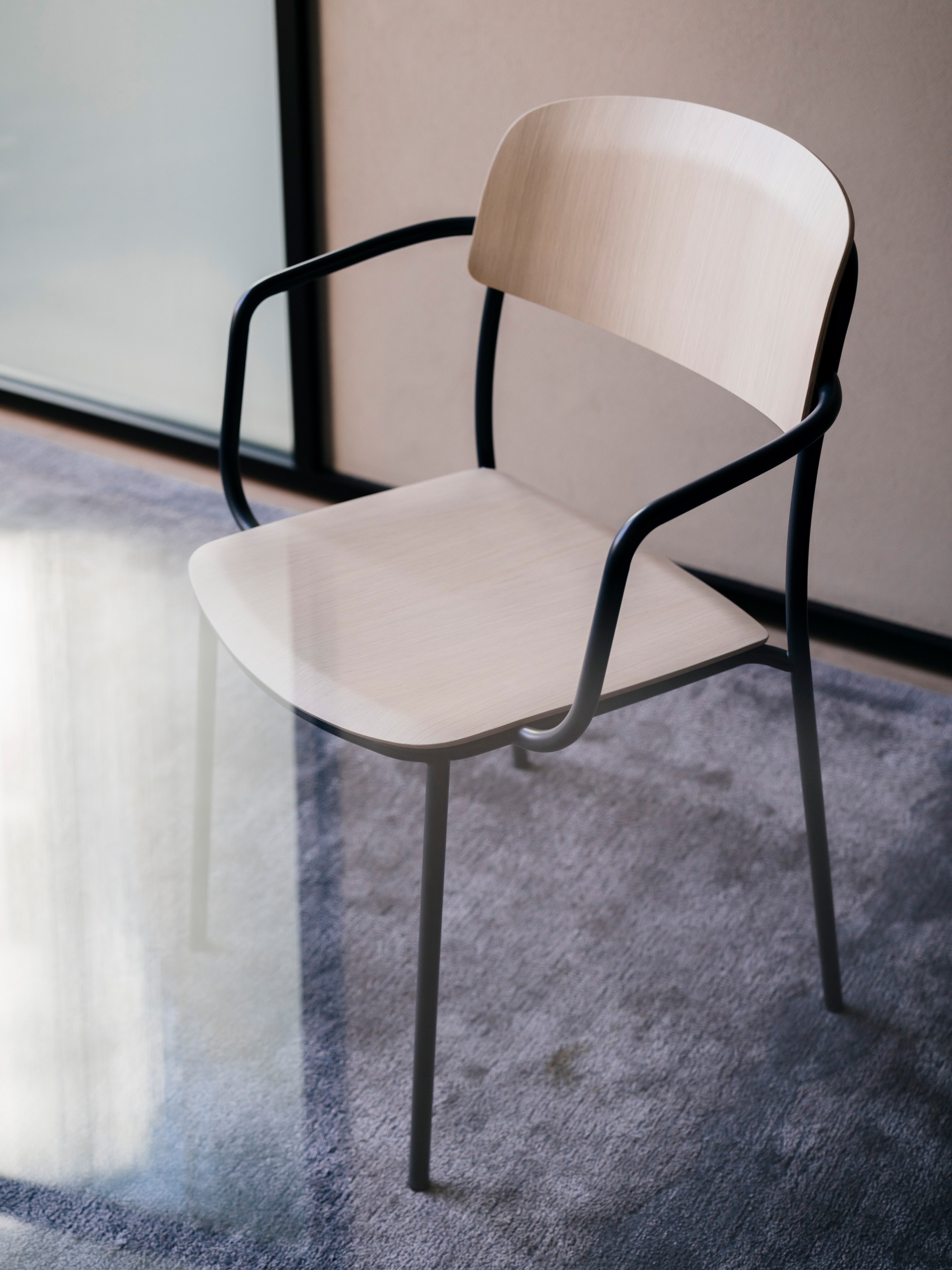 A chair with dark steel frames and light wood seats and backrests. A lens flare adds a dreamy quality to the foreground.