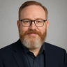 a man with a beard and glasses looks at the camera