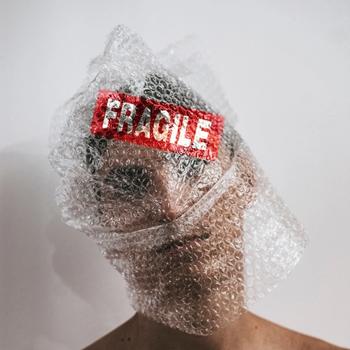 Man's face wrapped in bubble wrap with a Fragile sticker on his forehead.