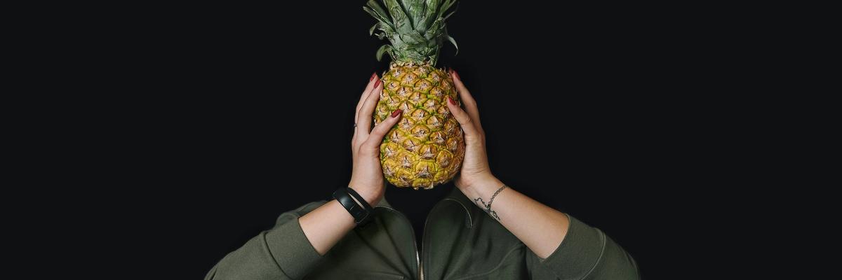 Person holding a pineapple infront of their face