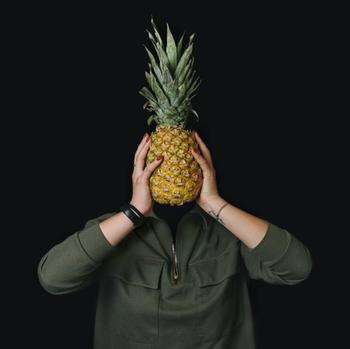 Person holding a pineapple infront of their face