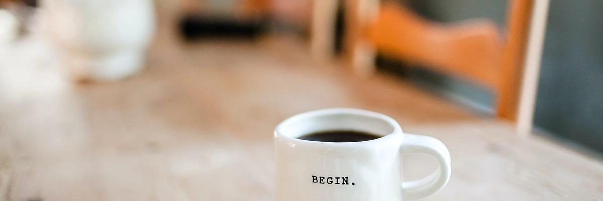 Coffee cup on a wooden table with the word BEGIN printed on the cup