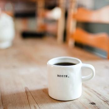 Coffee cup on a wooden table with the word BEGIN printed on the cup