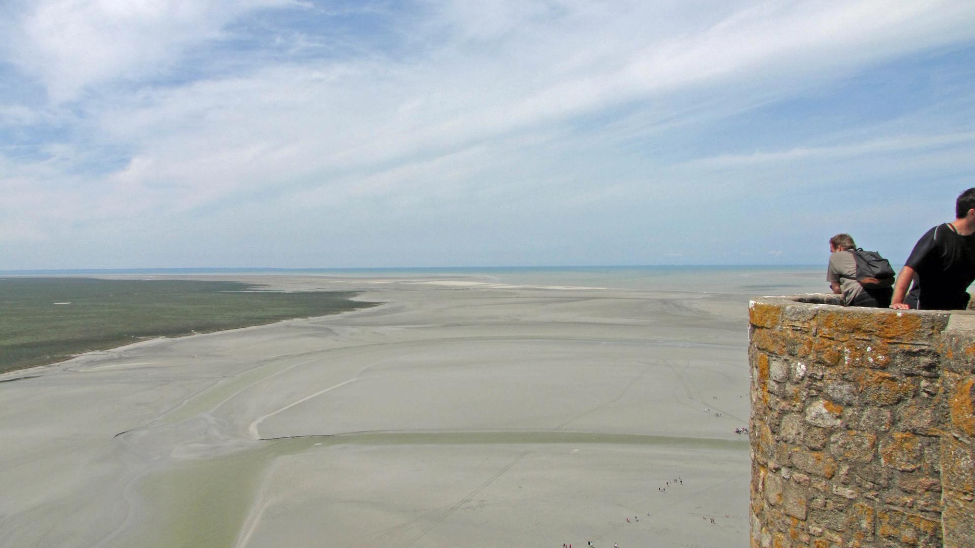Vue sur la baie du Mont-Saint-Michel à marée basse, avec la digue menant au village, un parcours accessible aux chiens tenus en laisse