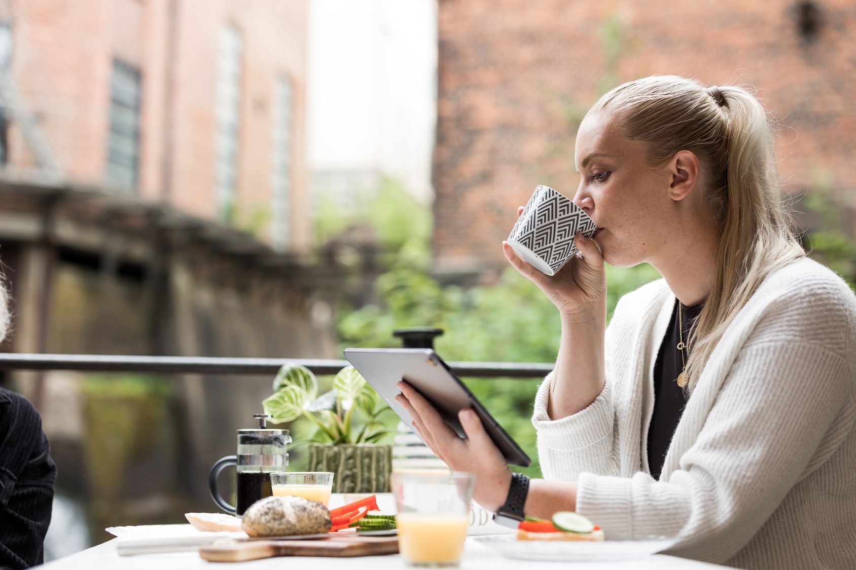 Två unga personer sitter vid frukostbordet på en terass och tittar på något roligt på en laptop.