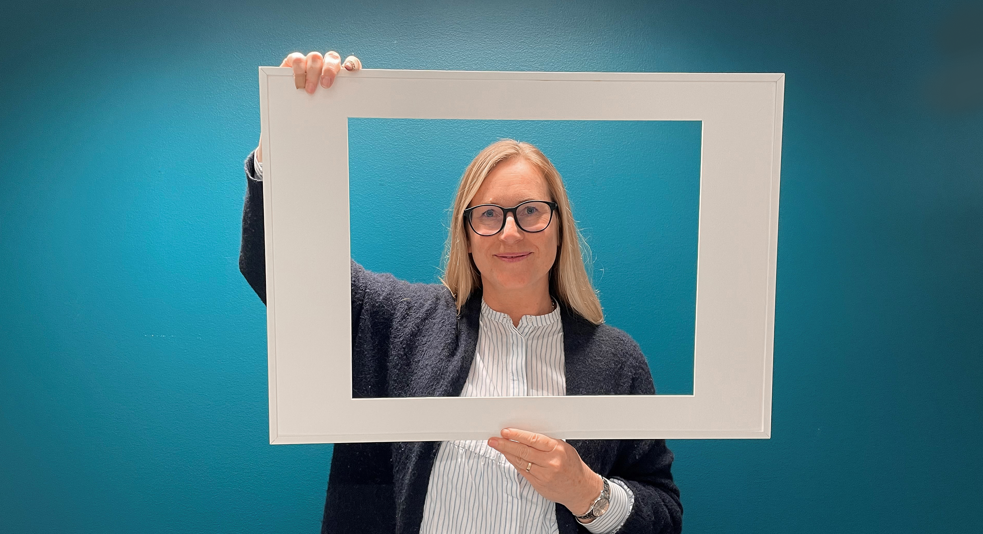 Susanna som jobbar på Sappa ler mot kameran genom en fotoram.