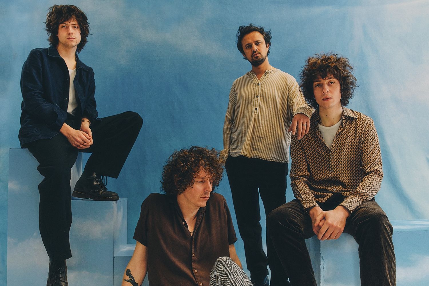 Mystery Jets stand together in a press photo against a dark red backdrop