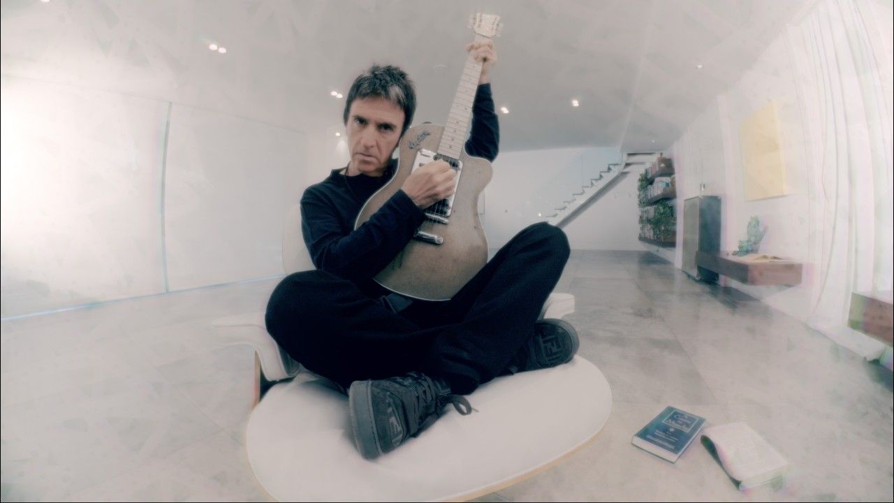 Johnny Marr Spin video image with Marr standing against a dark blue textured background.