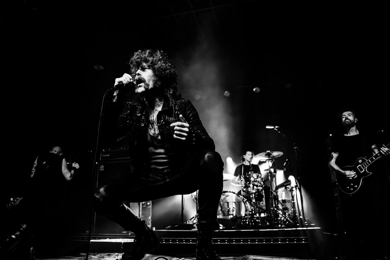 AFI performing live onstage in black and white, with Davey Havok crouched at the front holding a microphone.