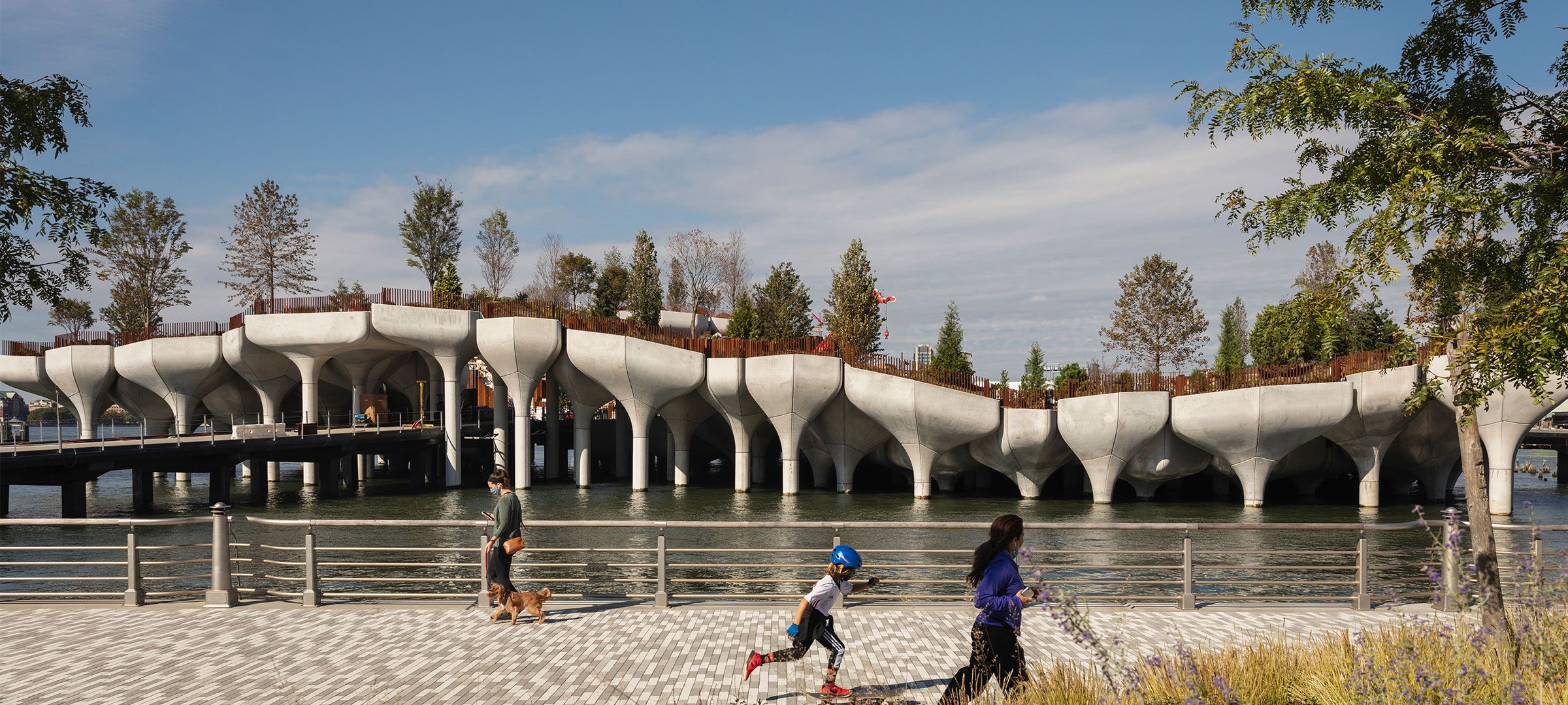 View of the Little Island pots from the Hudson River Park esplanade, with people walking in the foreground