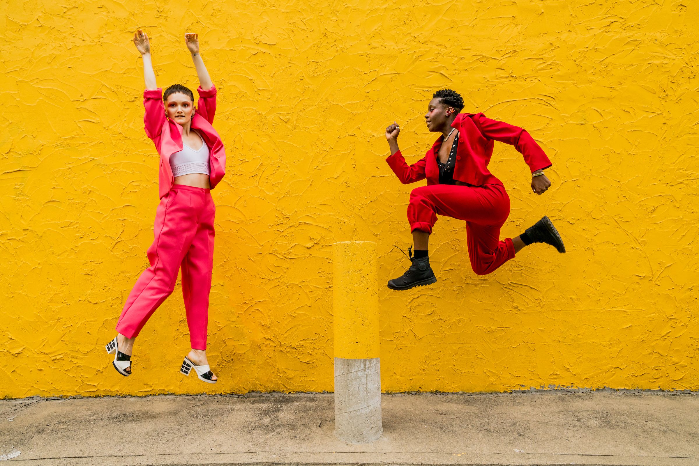 Two people dressed in red jumping in the air in front of a bright yellow wall