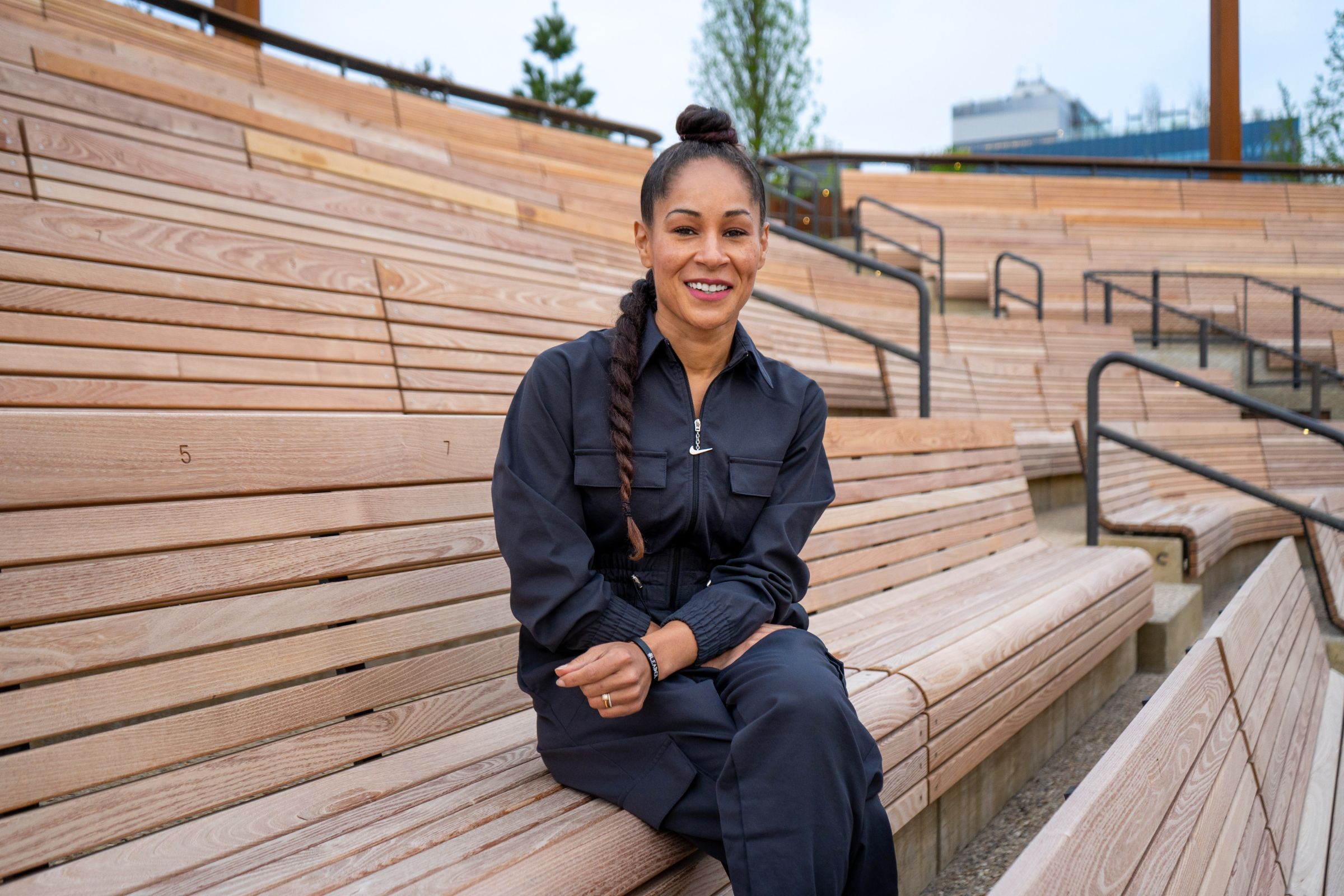 A woman sitting with her legs crossed on a wooden bench in an outdoor theater