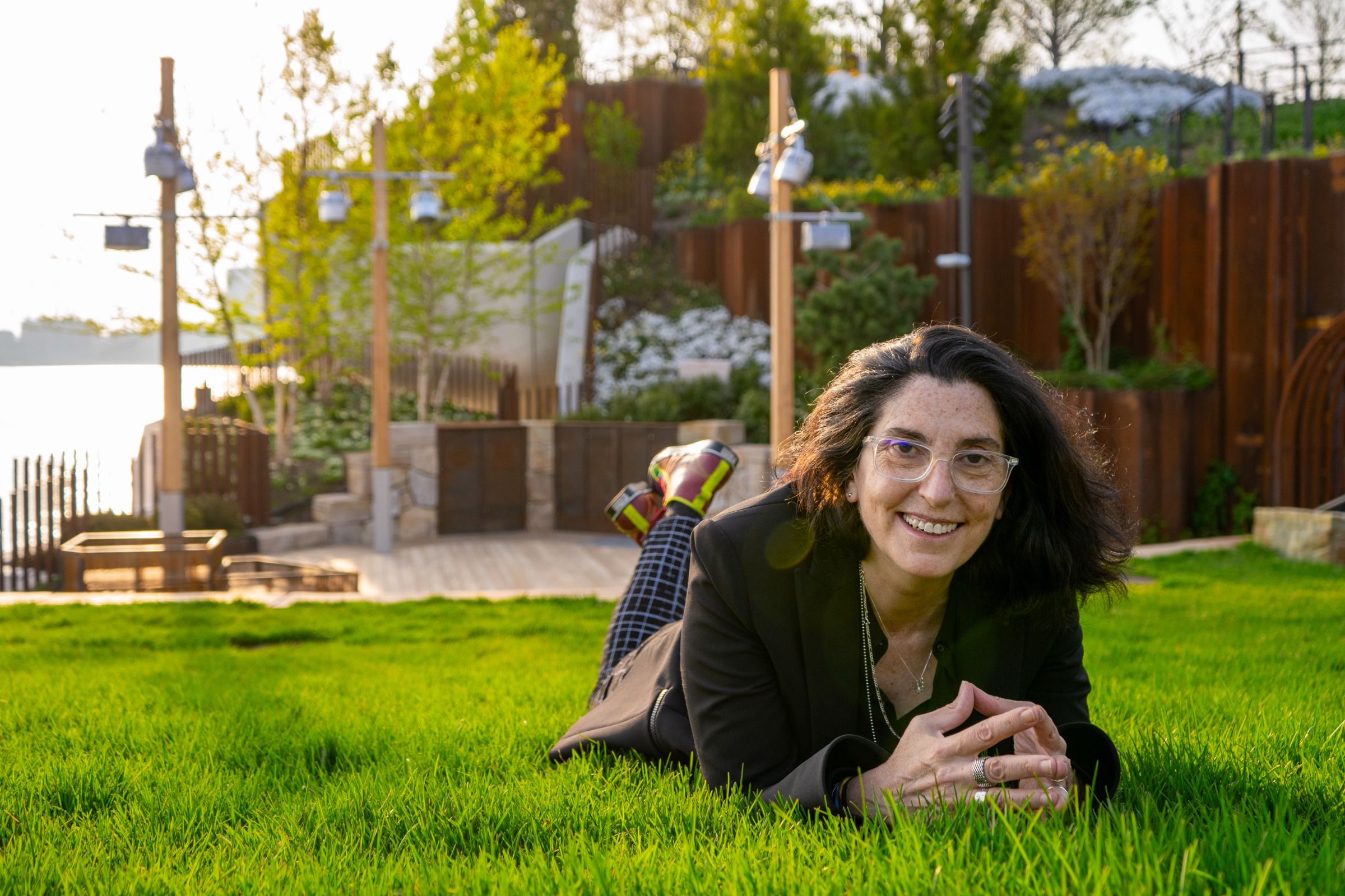 A woman laying down on in the grass propped up on her elbows, with a small wooden stage in the background