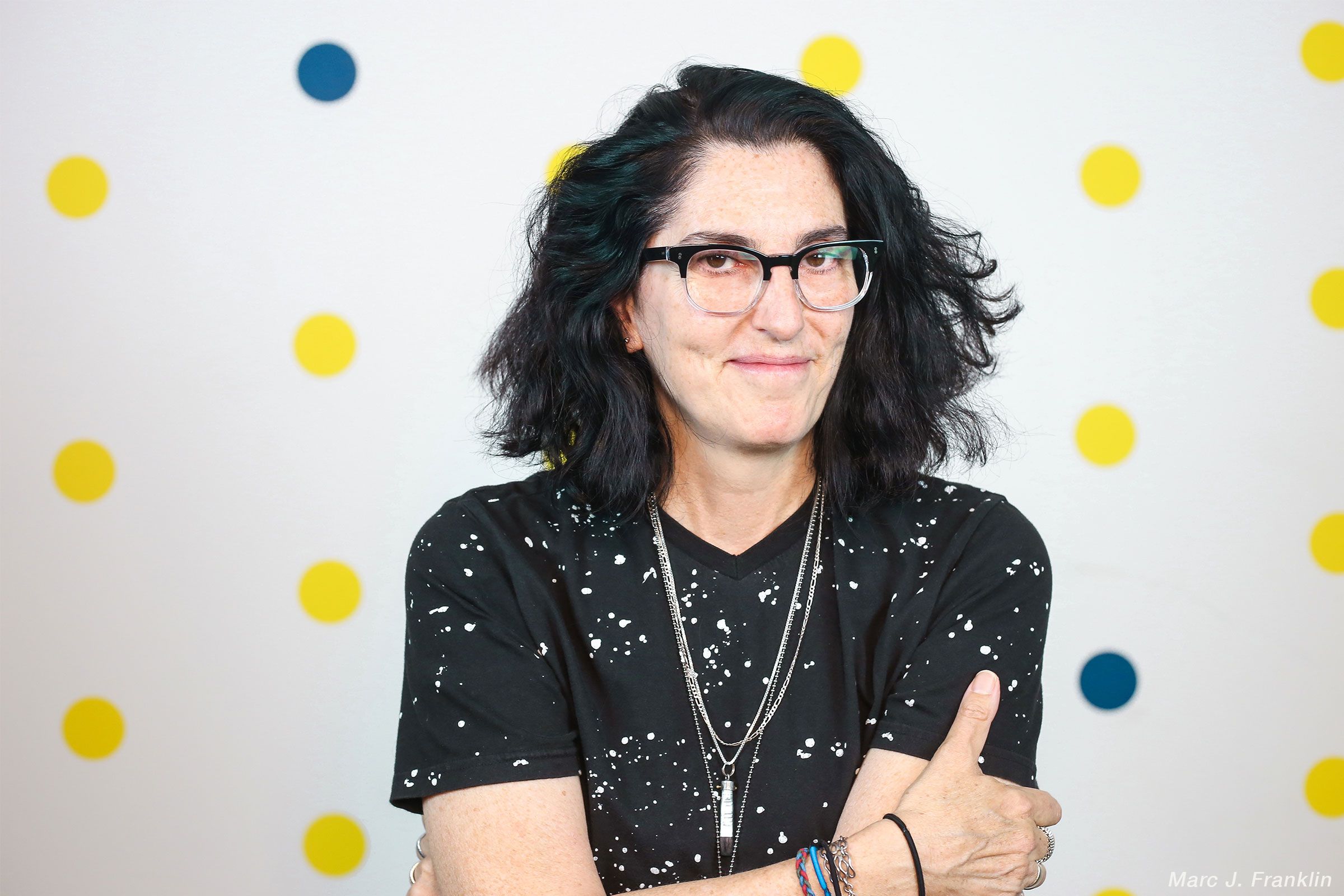 A close-up of a woman with dark hair, wearing glasses.