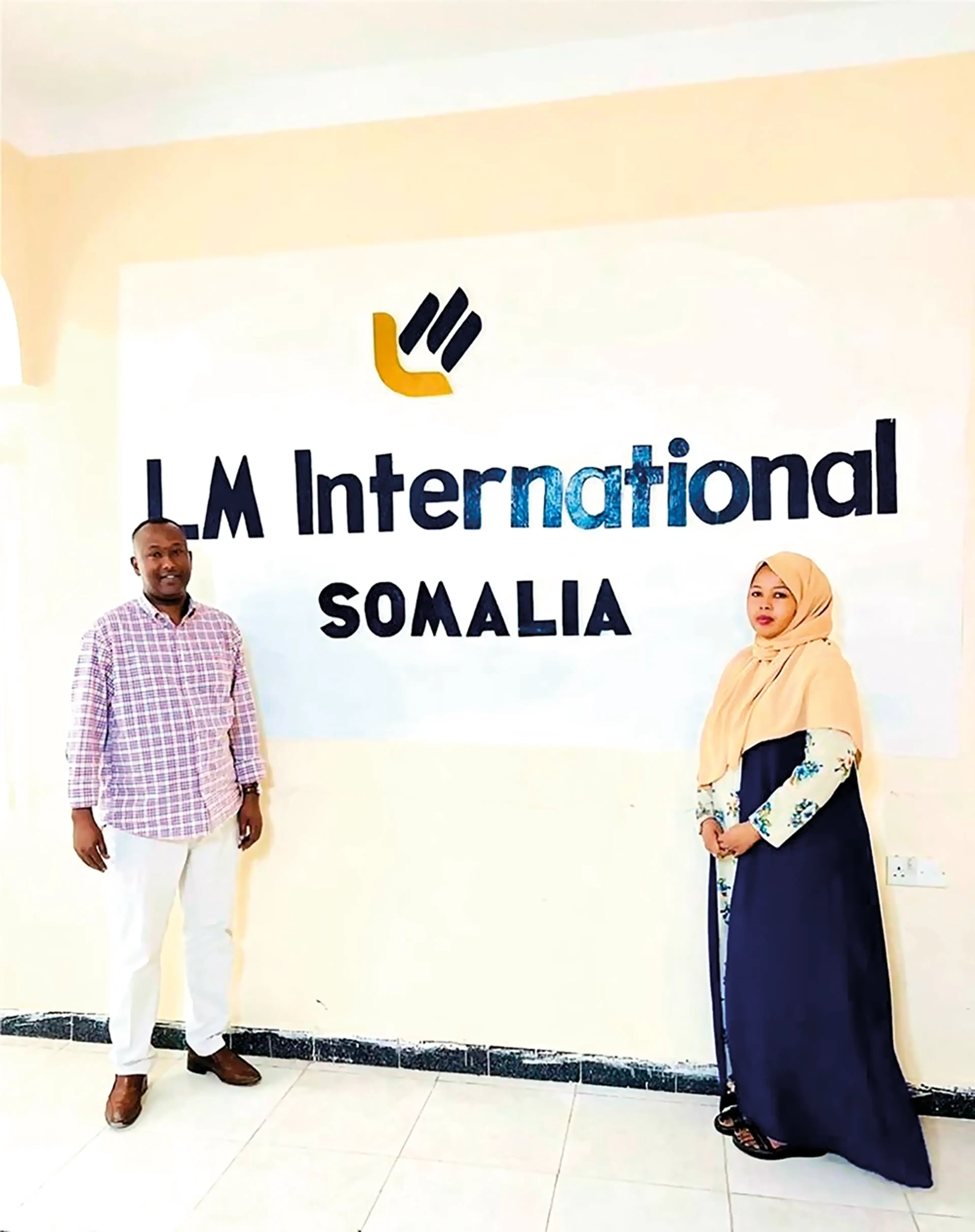 Layla Artan och en man står framför en skylt där det står LM International Somalia,