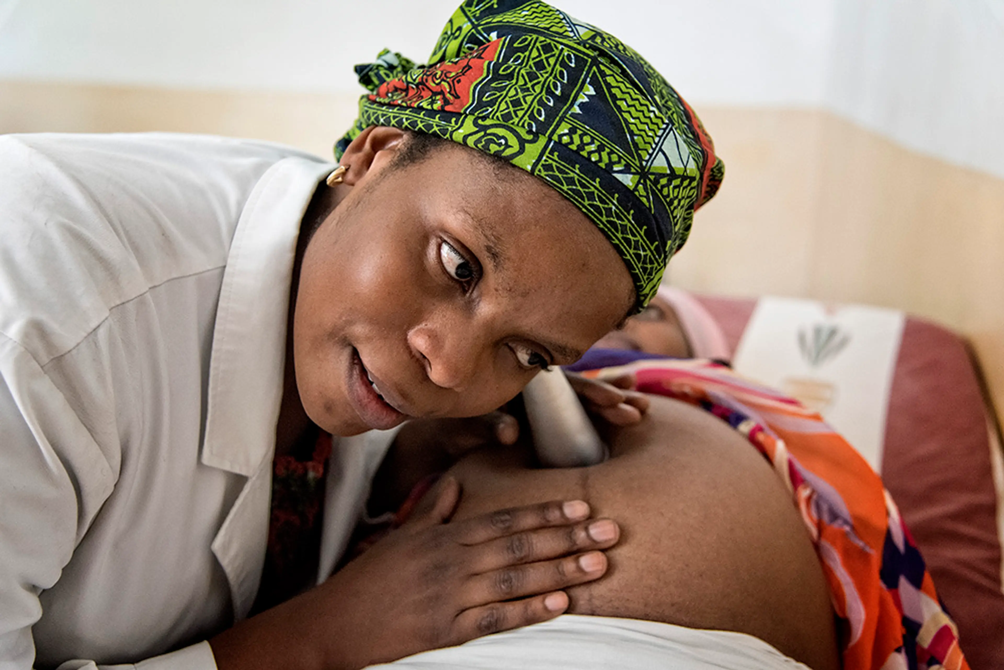Afrikansk barnmorska lyssnar på gravid kvinnas mage