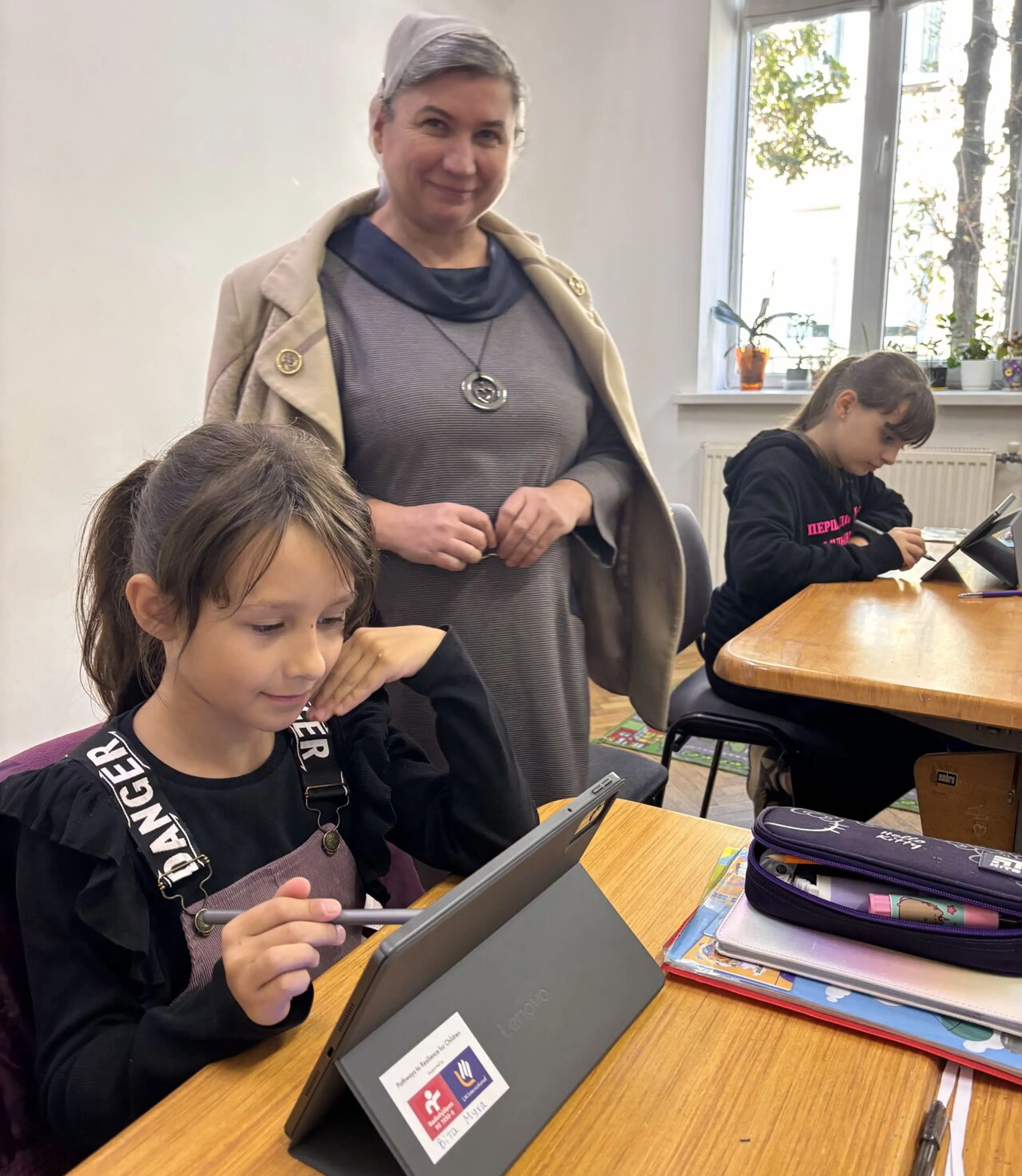 Flicka i klassrum som arbetar med suftplatta, kvinna står bredvid