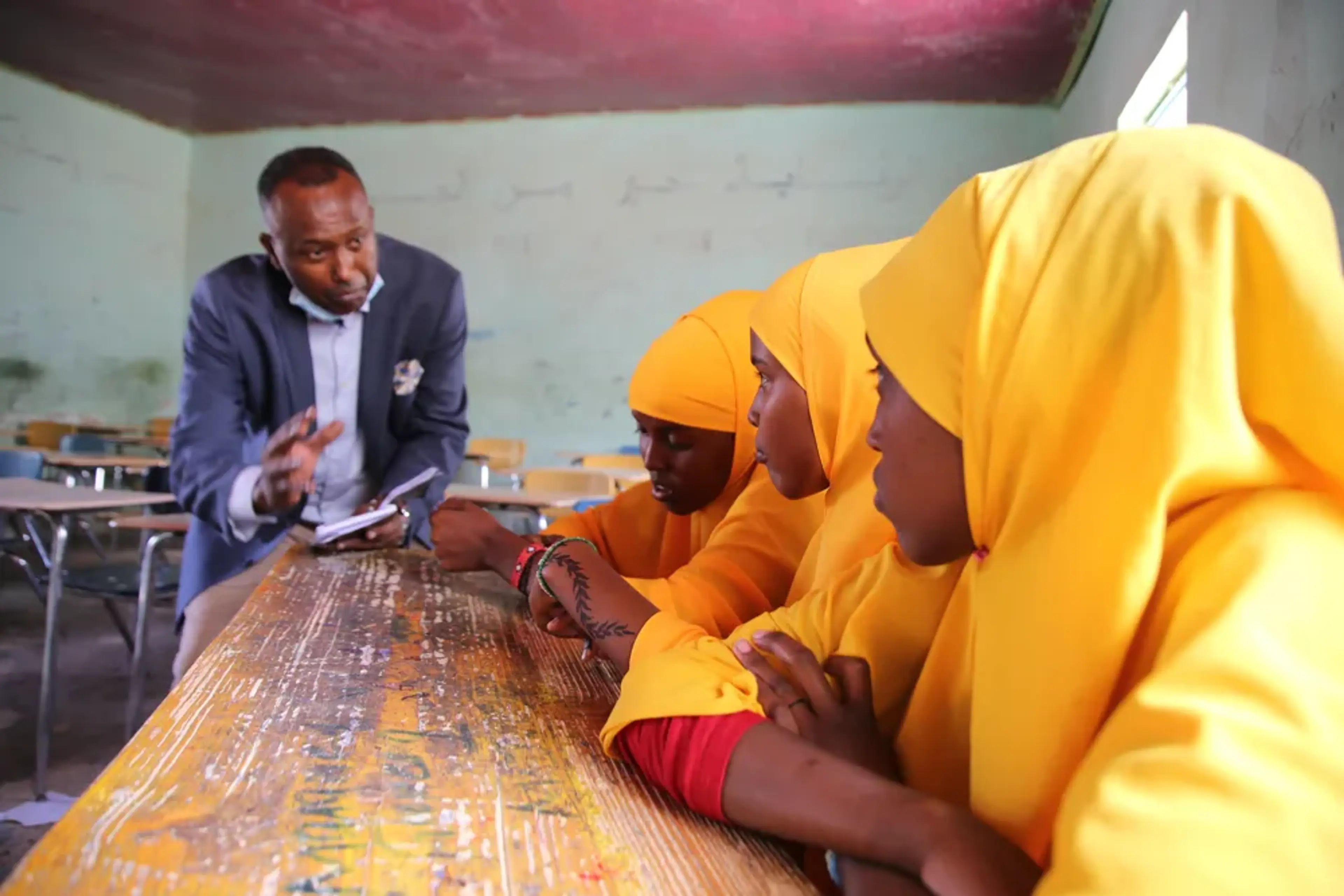 Tre flickor sitter vid ett bord i skolan i Somalia och lyssnar på sin lärare