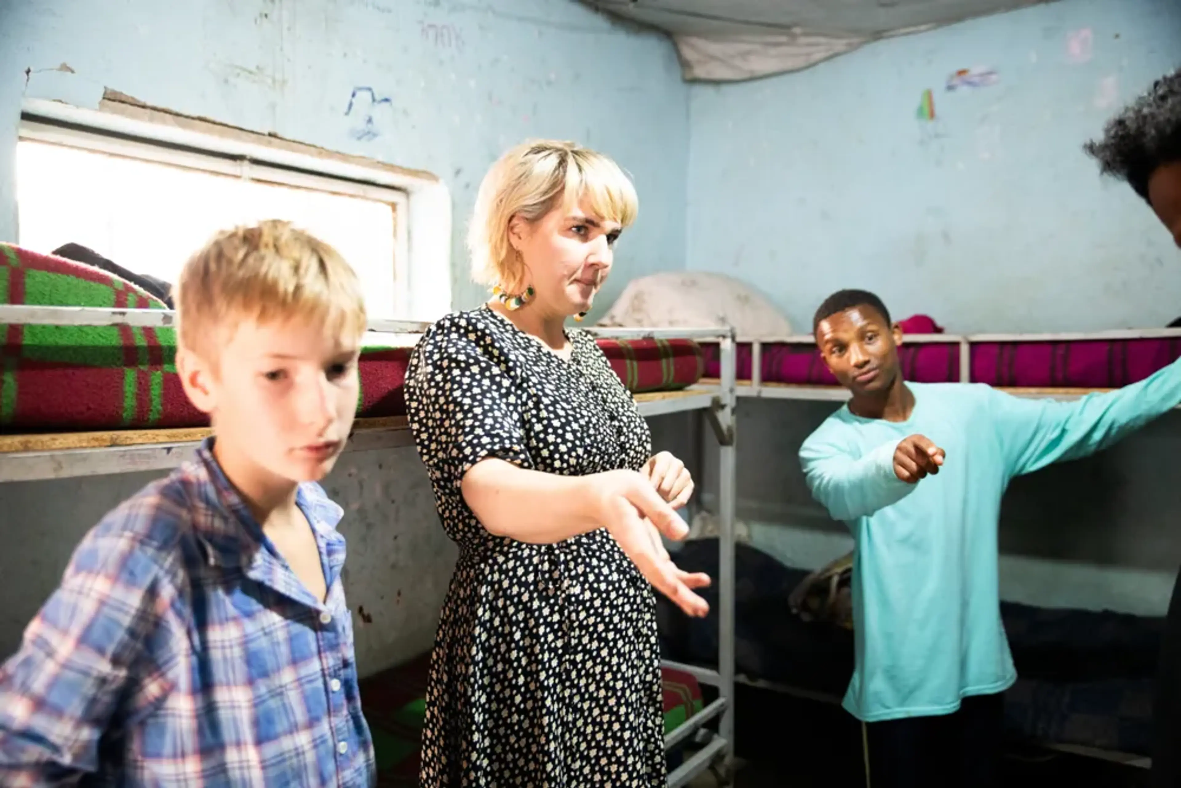 Clara och hennes son står och pratar engagerat med en ung man som pekar i ett rum med våningsängar