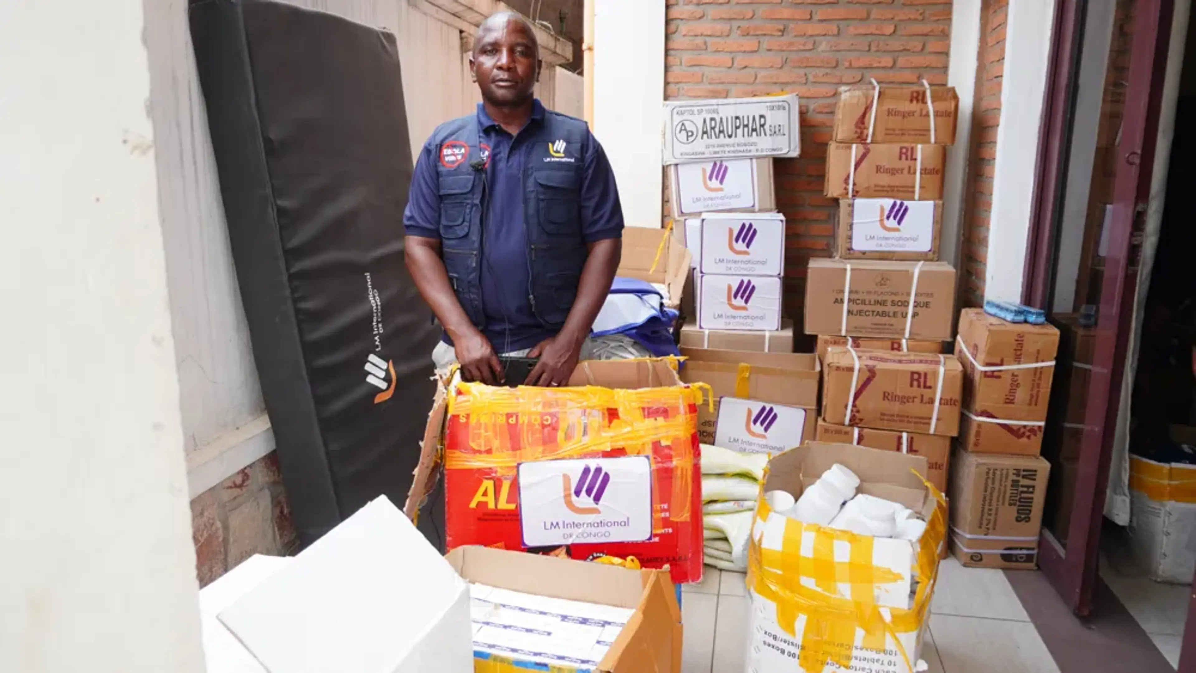 Erasto Ngulu Ndibito står framför lådor med sjukvårds- och hygienmaterial vid Pinga-sjukhuset.