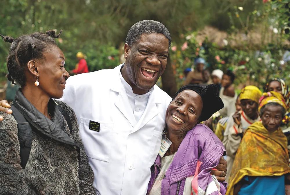 Denis Mukwege i en läkarrock skrattar tillsammans med två kvinnor