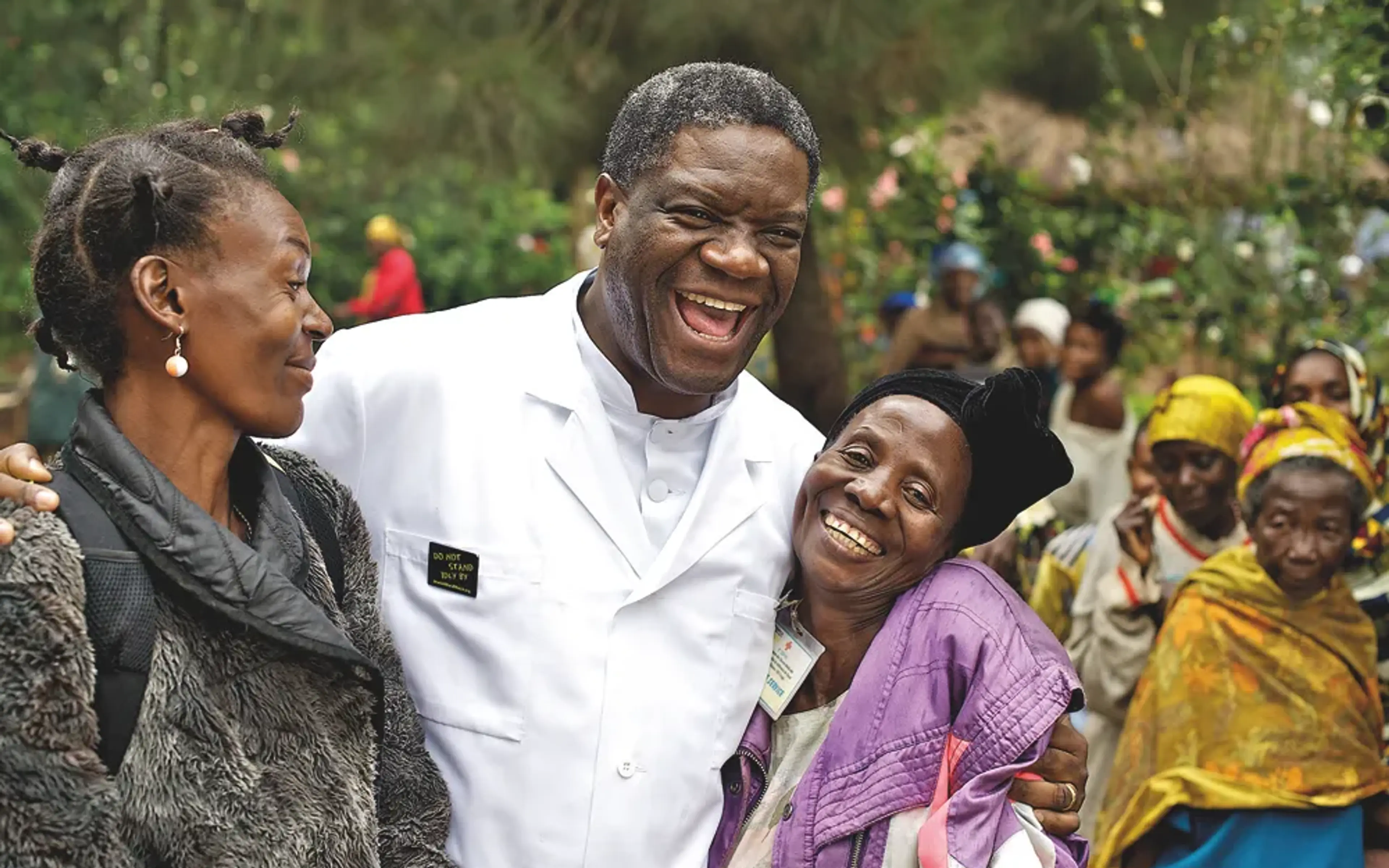 Denis Mukwege i en läkarrock skrattar tillsammans med två kvinnor