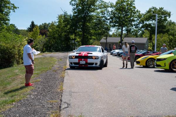 White and red Dodge Challenger Hellcat pulling out of the car show. 