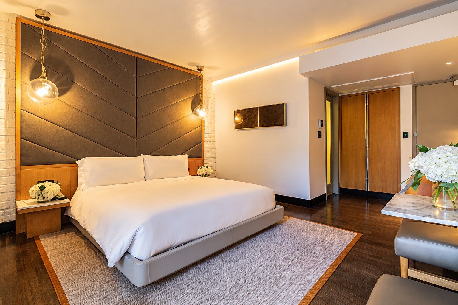 A hotel room with a king-sized bed, two nightstands, and pendant lights