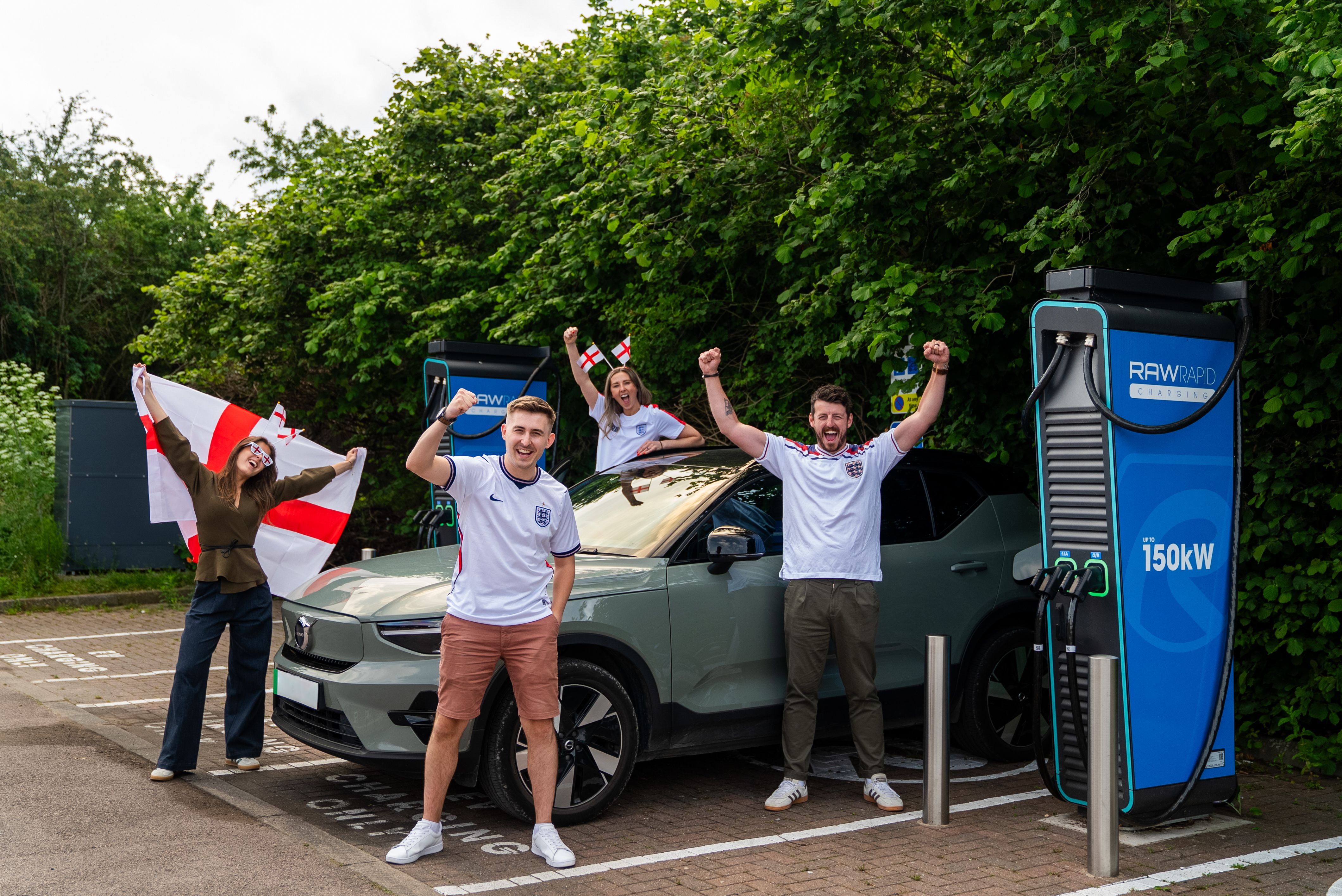 A group of friends pose with England flags by a RAW Rapid EV charger