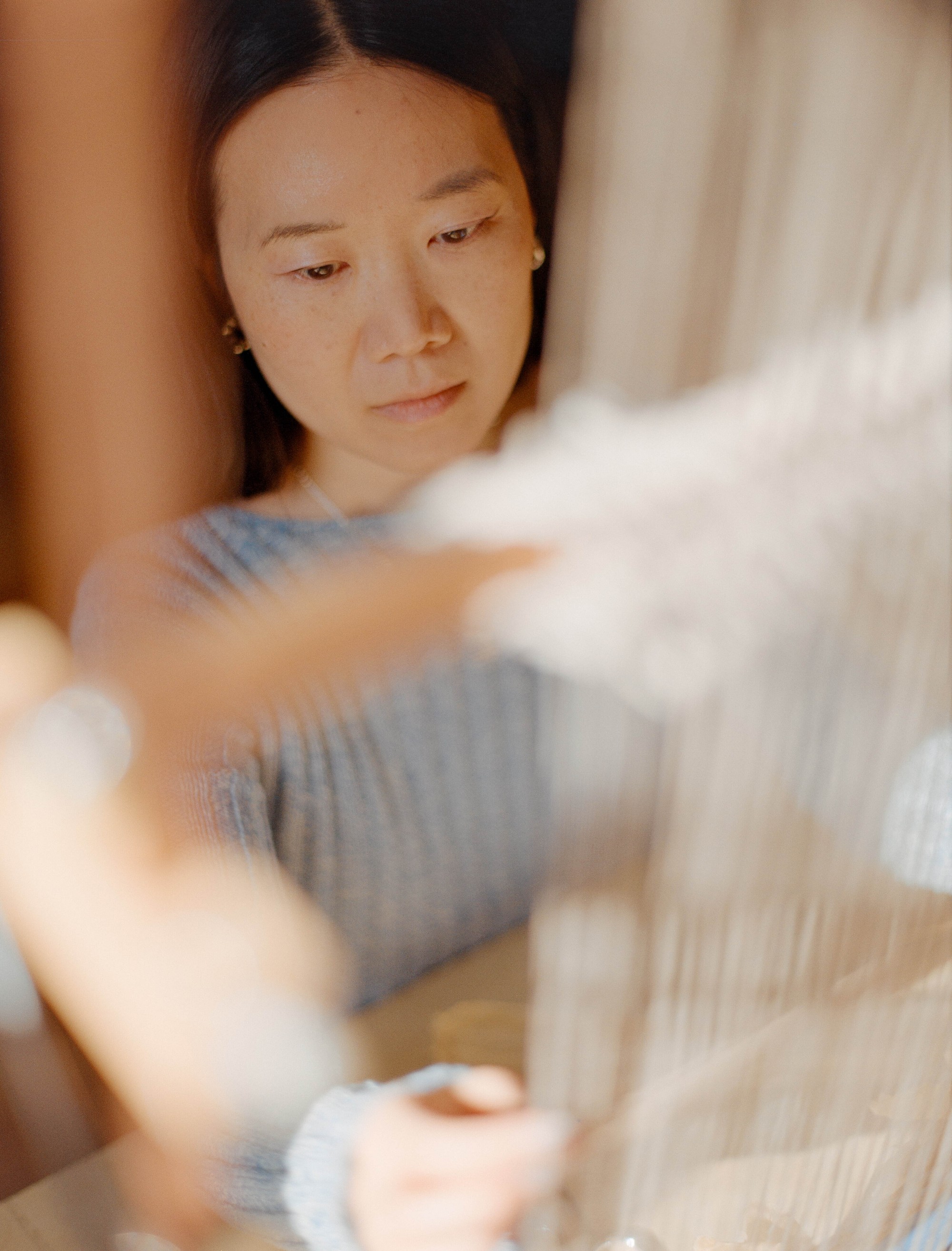 Laura Kung weaving at her loom seen between the warp threads in her Portland studio, shot on medium format film by Nathaniel Perales