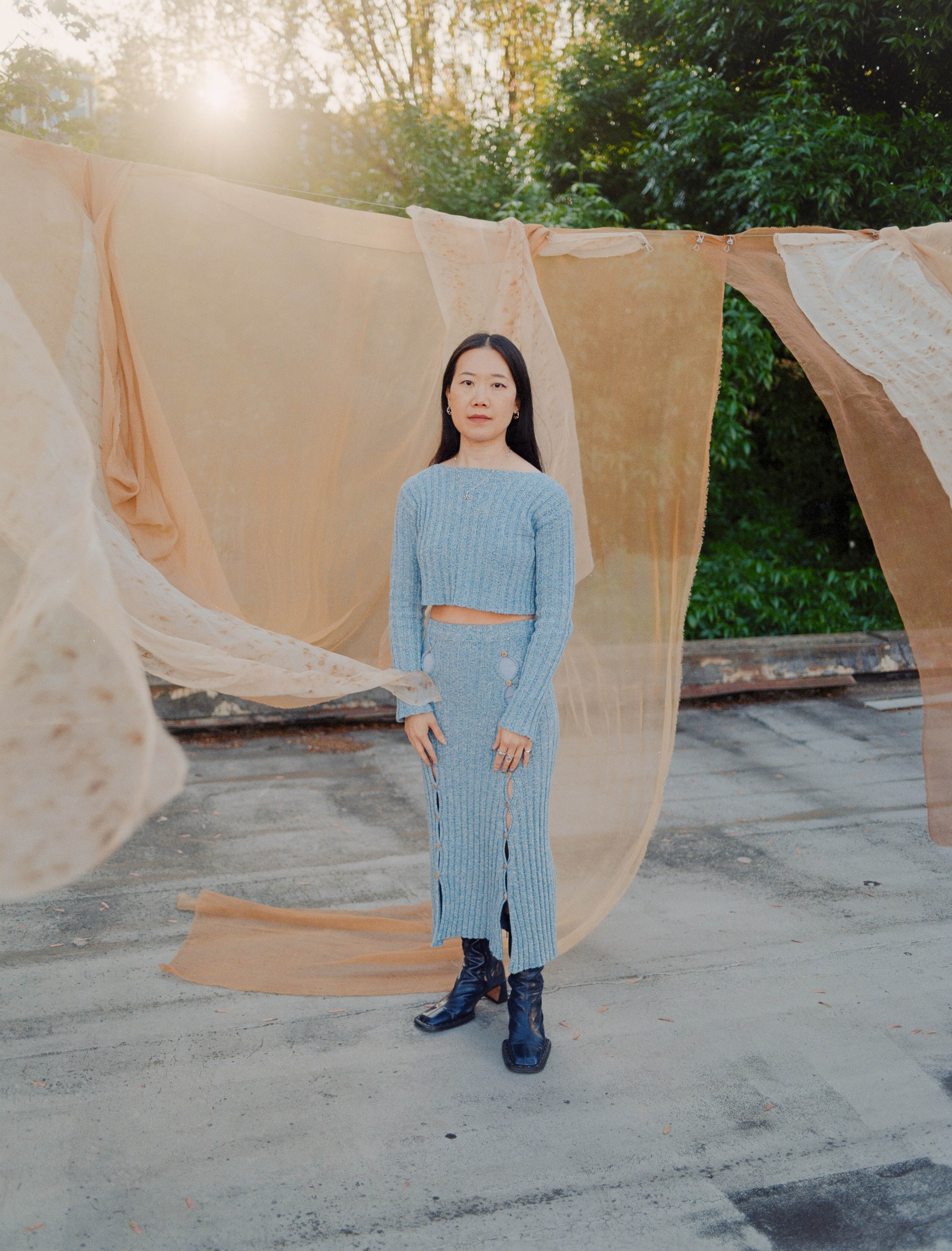 Full-length golden hour portrait of Portland textile artist Laura Kung between lengths of naturally dyed fabric on a rooftop, medium format film by Nathaniel Perales