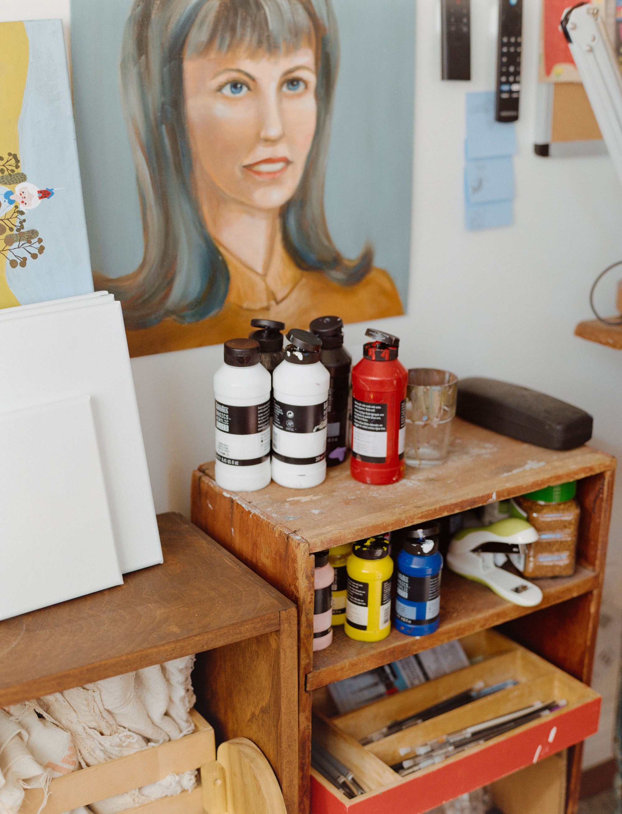 Acrylic paint bottles and canvases beside a portrait painting in Burger Babie artist Addeline Griswold's Los Angeles studio, medium format film photograph