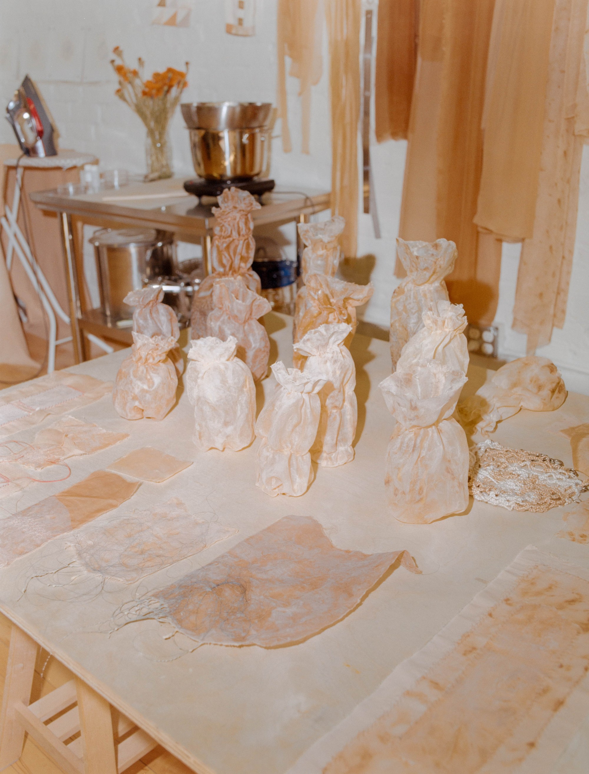 Naturally dyed fabric bundles arranged on a studio table with dye equipment behind, Portland artist Laura Kung, medium format film
