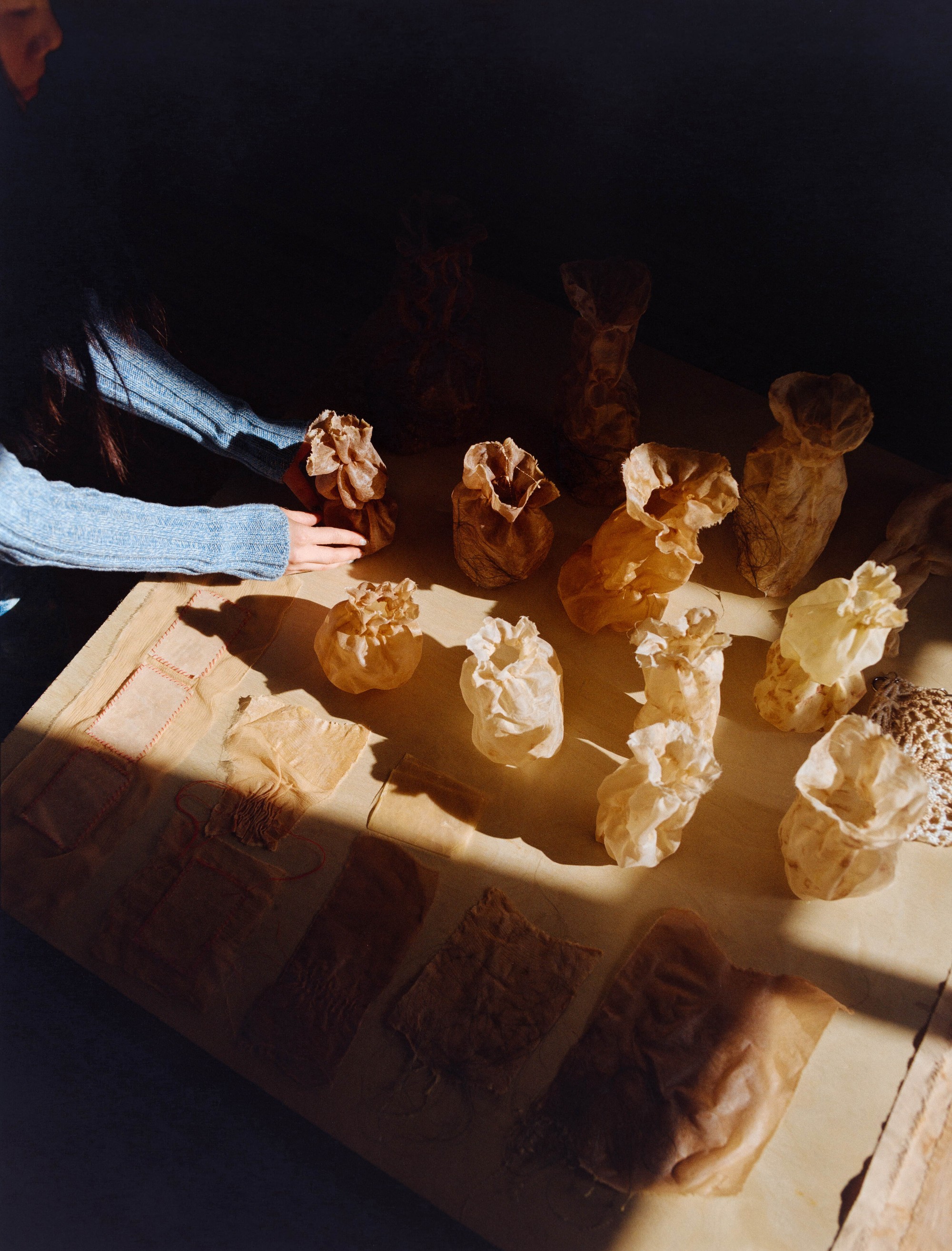 Overhead view of Laura Kung arranging naturally dyed fabric bundles in studio light, Portland artist, medium format film by Nathaniel Perales