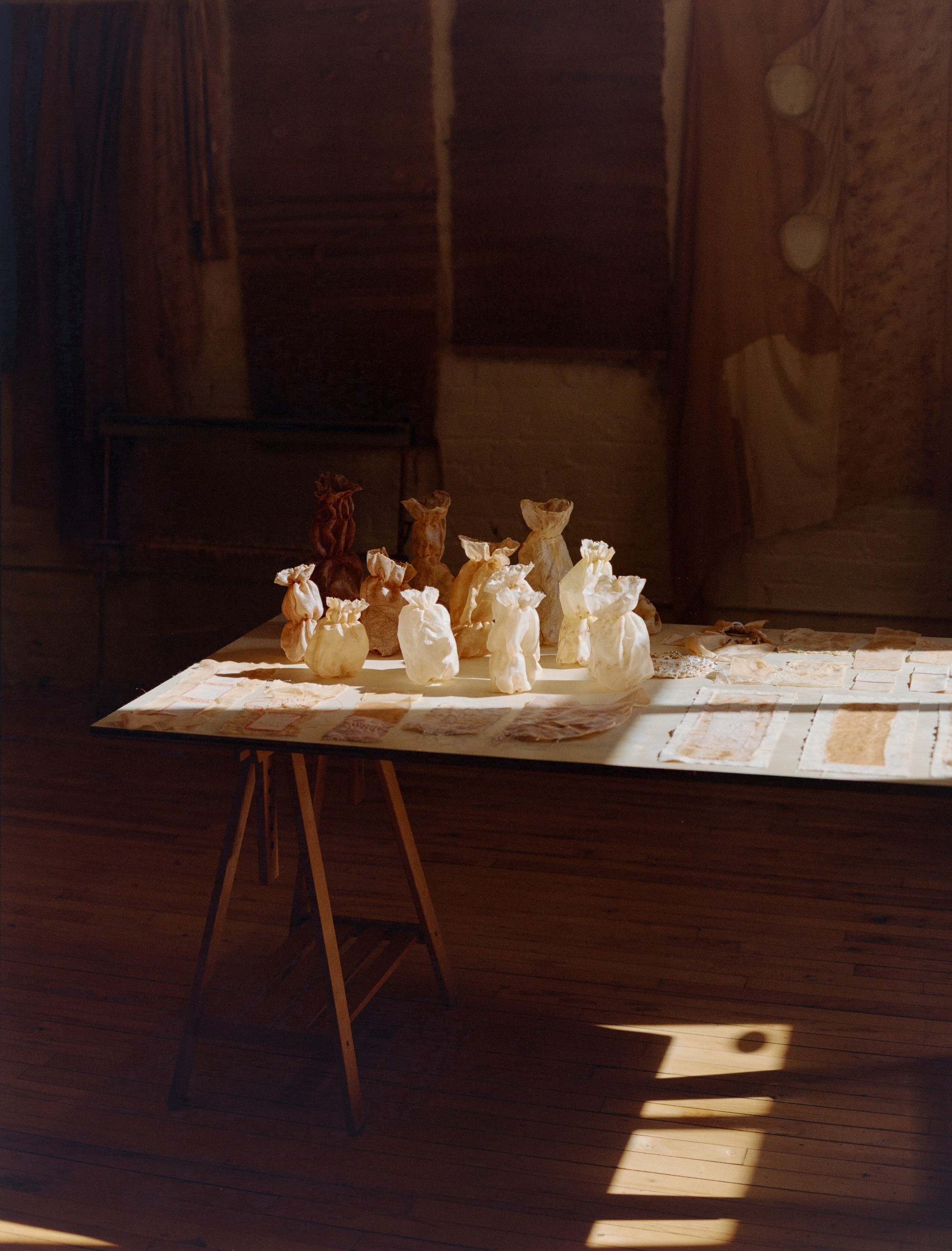 Dyed fabric bundles and textile works arranged on a studio table in raking light, Portland artist Laura Kung, medium format film by Nathaniel Perales
