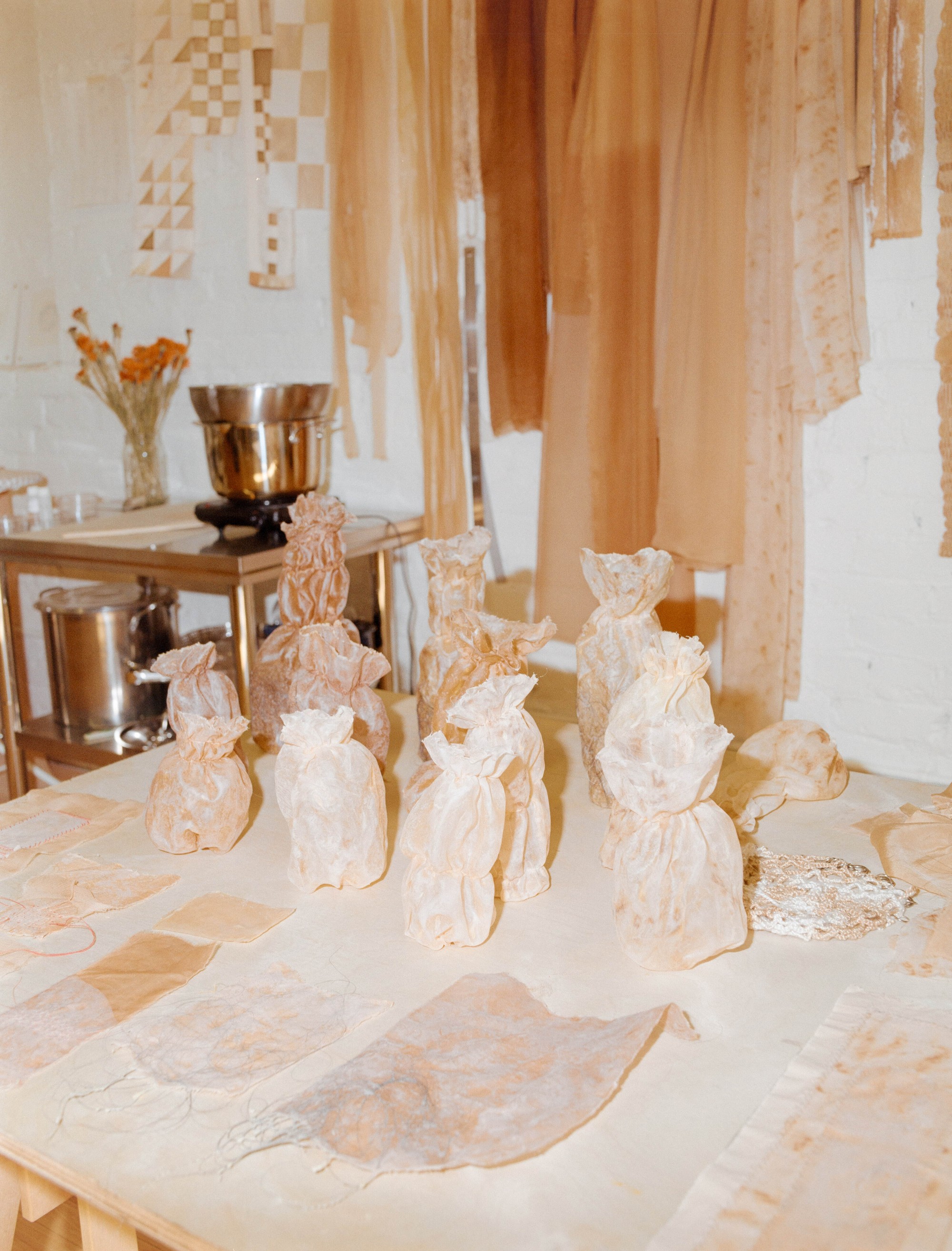 Naturally dyed fabric vessels on a studio table with dye pot and hanging dyed cloth behind, Portland artist Laura Kung, medium format film