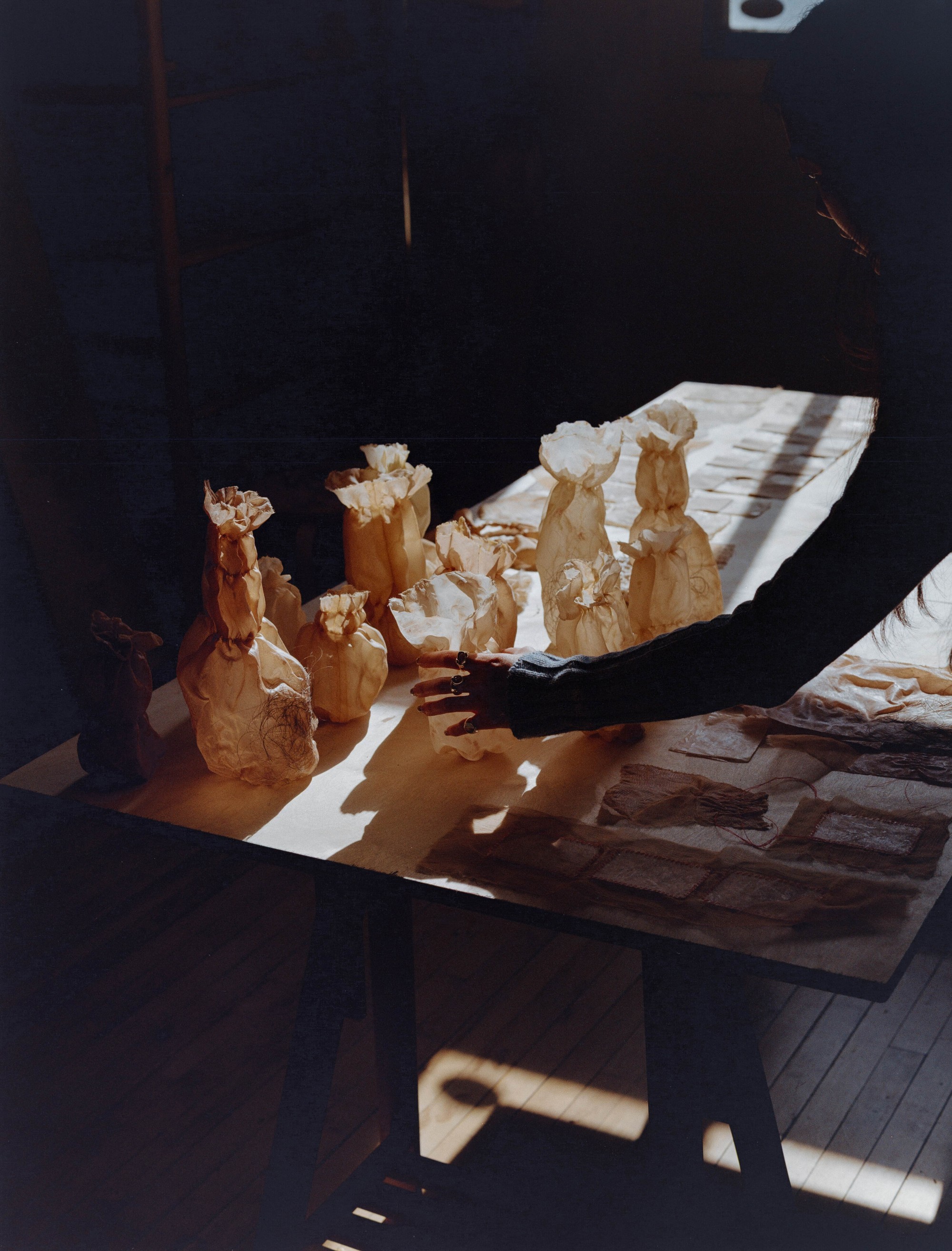 Laura Kung reaching toward naturally dyed fabric vessels in a shaft of studio light, Portland artist, medium format film by Nathaniel Perales