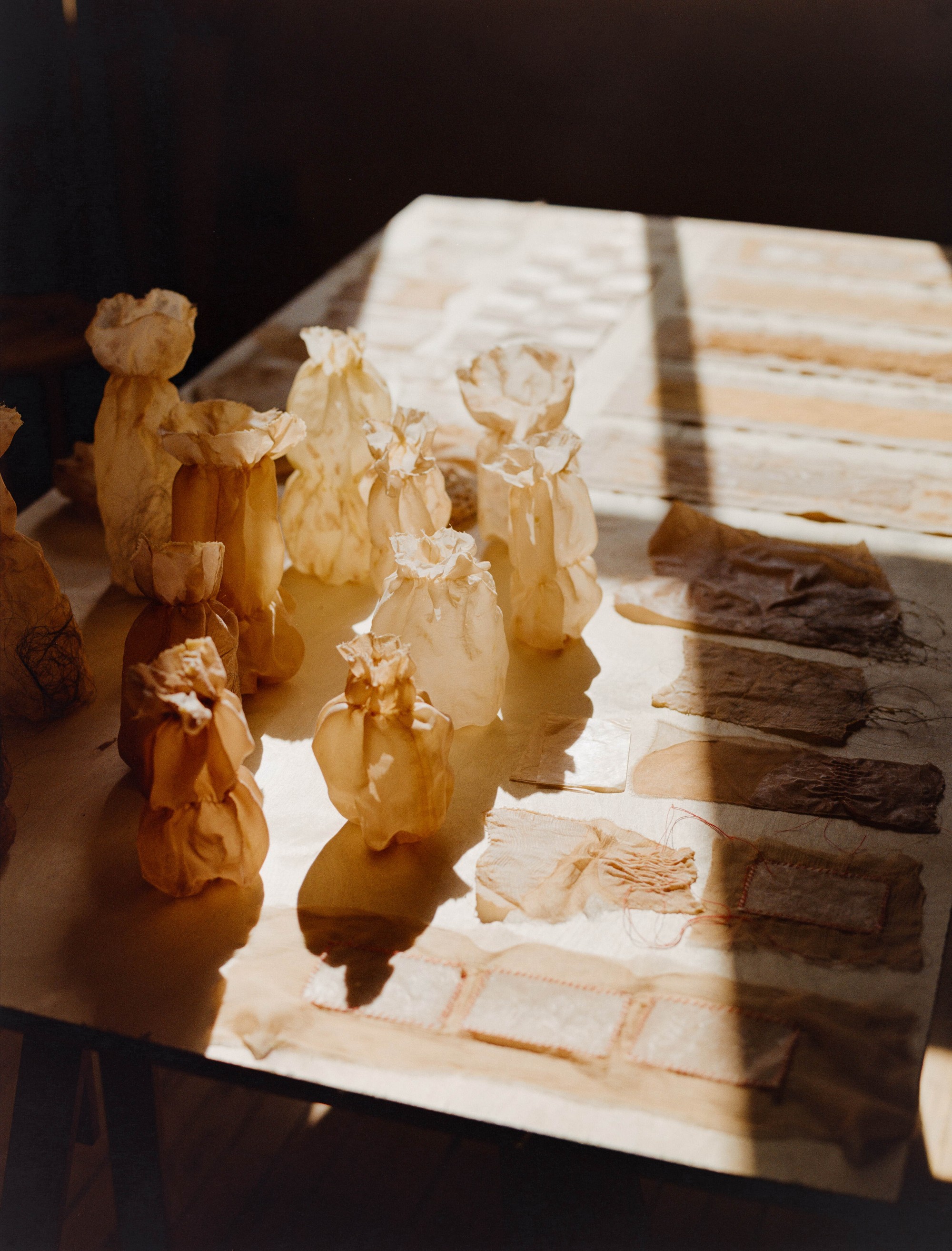 Naturally dyed fabric bundles and textile samples in afternoon light on a studio table, Portland artist Laura Kung, medium format film