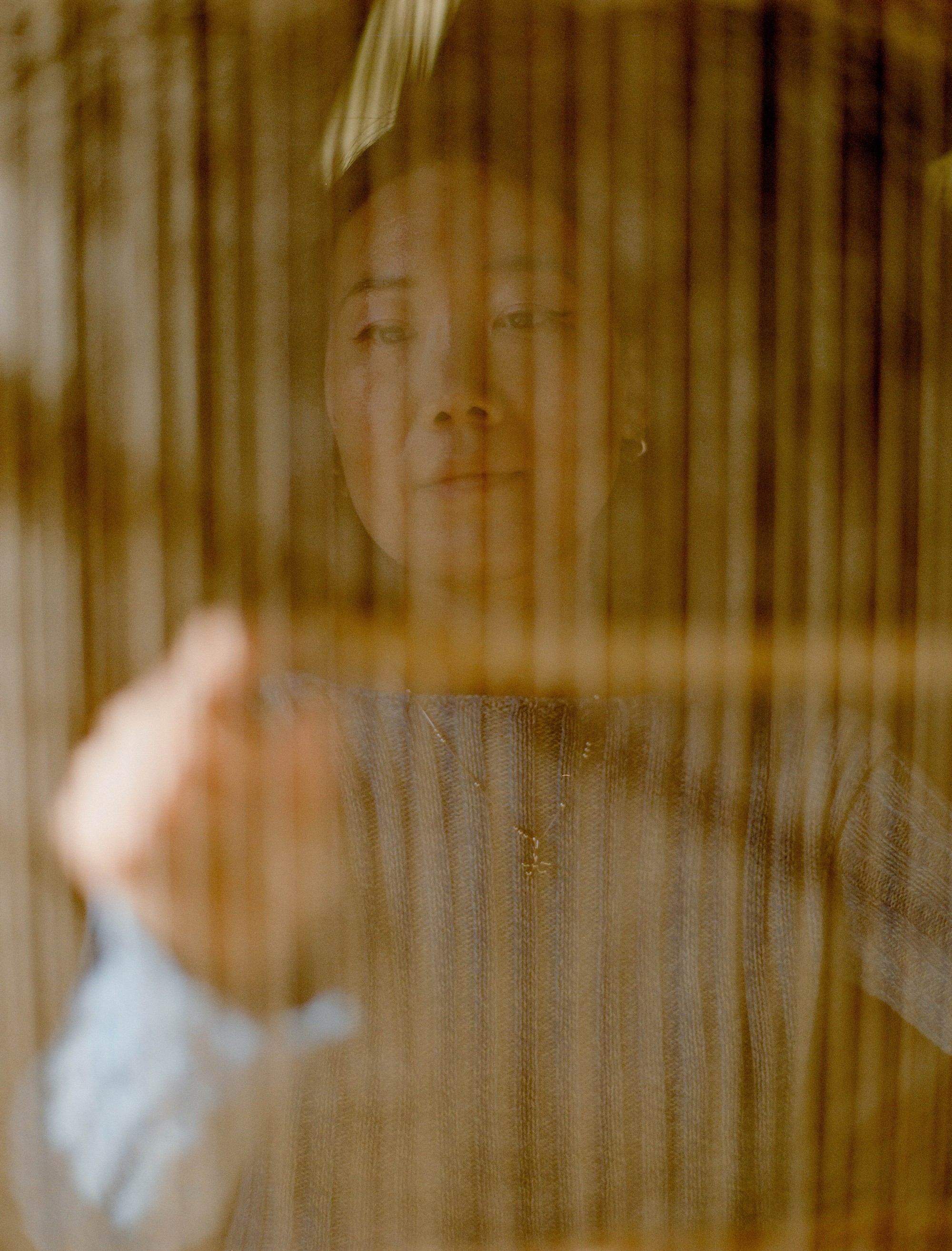 Portrait of Portland textile artist Laura Kung seen through hanging dyed warp threads in her studio, medium format film by Nathaniel Perales