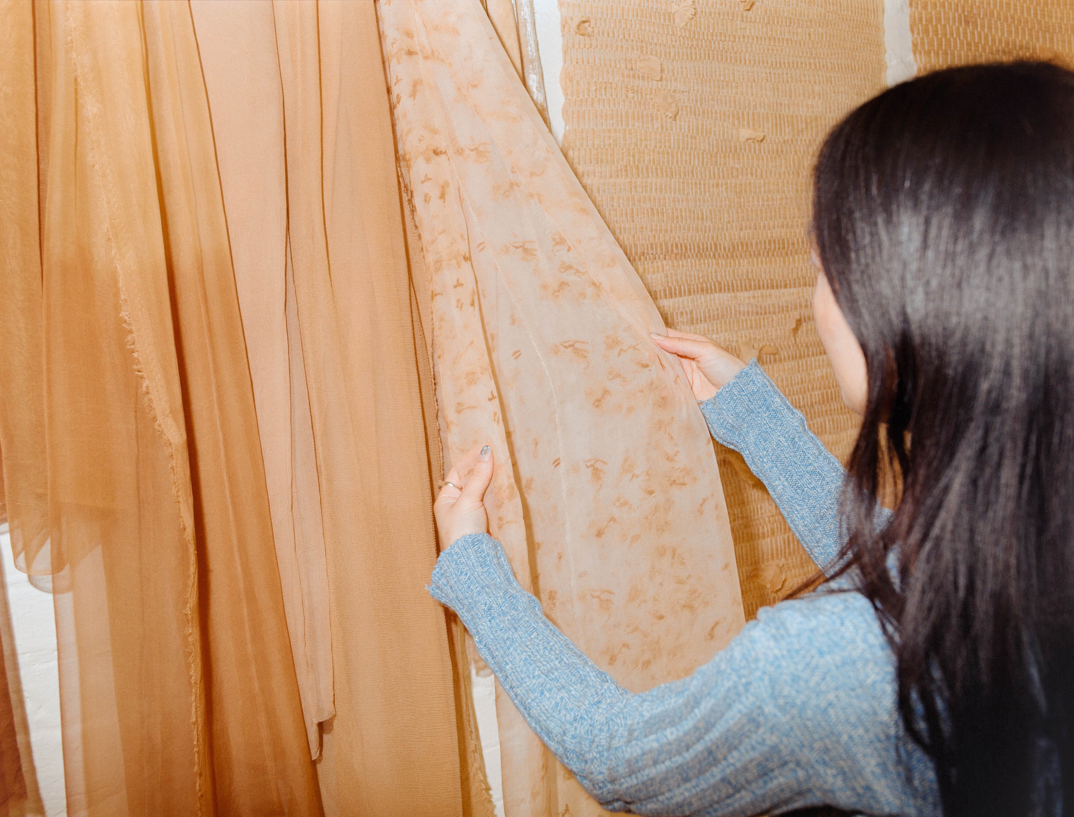 Laura Kung examining naturally dyed sheer fabric hanging in her Portland studio, shot on medium format film by Nathaniel Perales