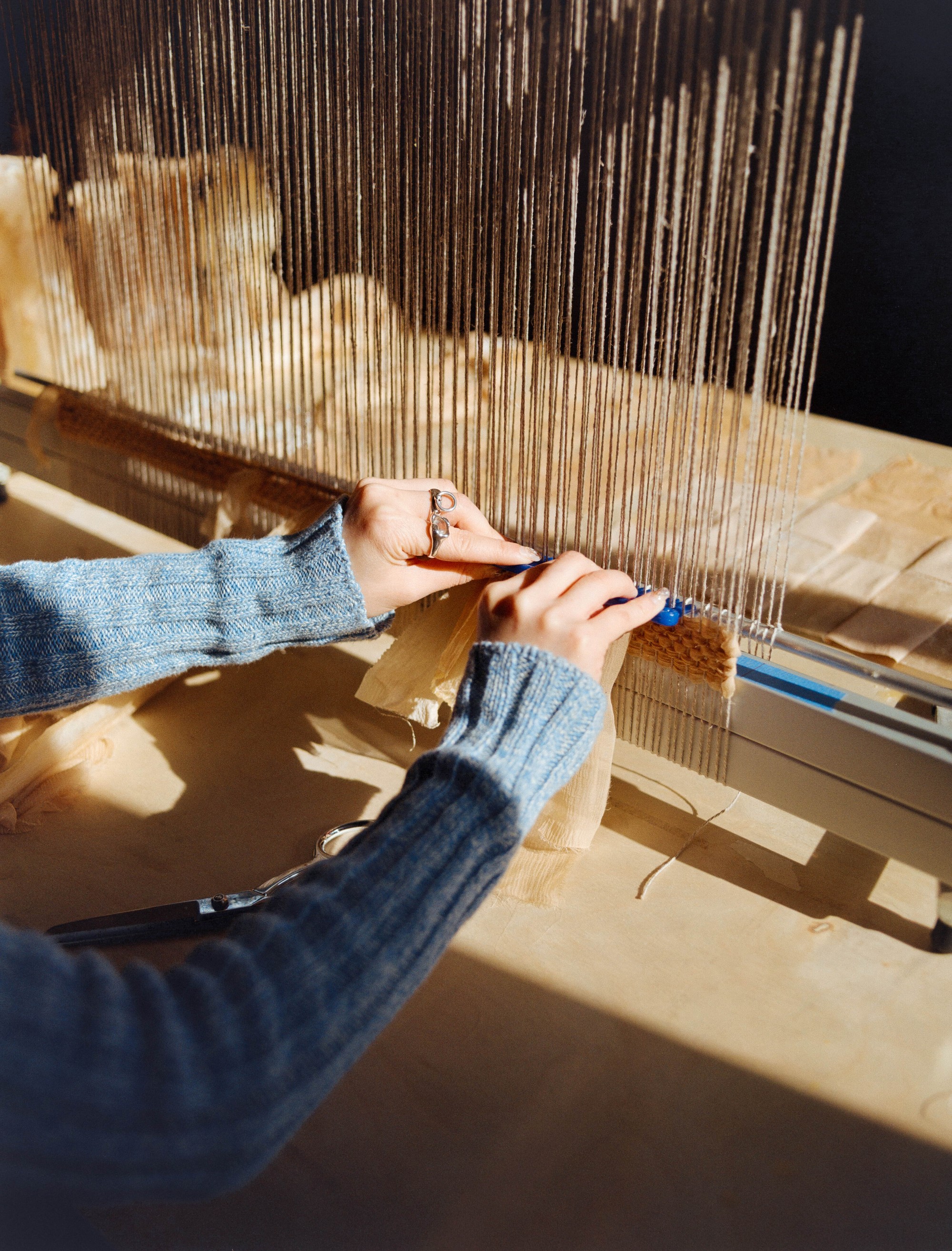 Laura Kung's hands weaving naturally dyed fiber into a textile on the loom, Portland studio, shot on medium format film by Nathaniel Perales