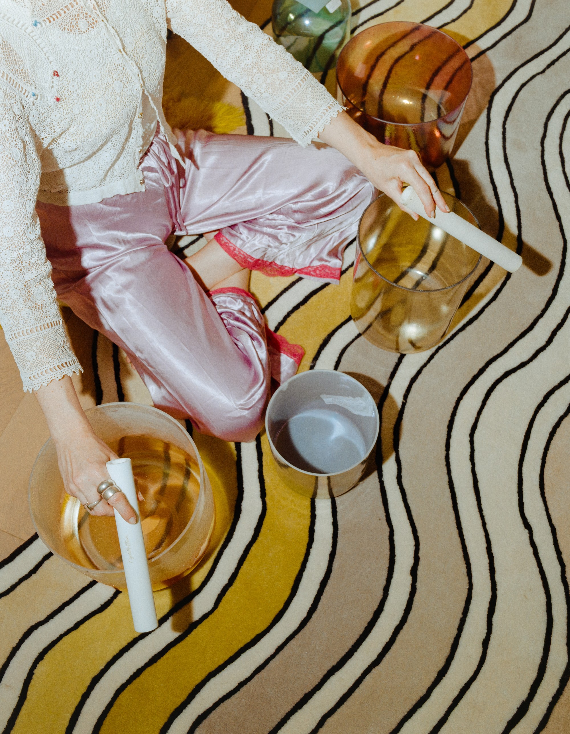 Overhead view of Allison Bagg with crystal singing bowls on a wavy patterned rug, shot on medium format film in Los Angeles by Nathaniel Perales