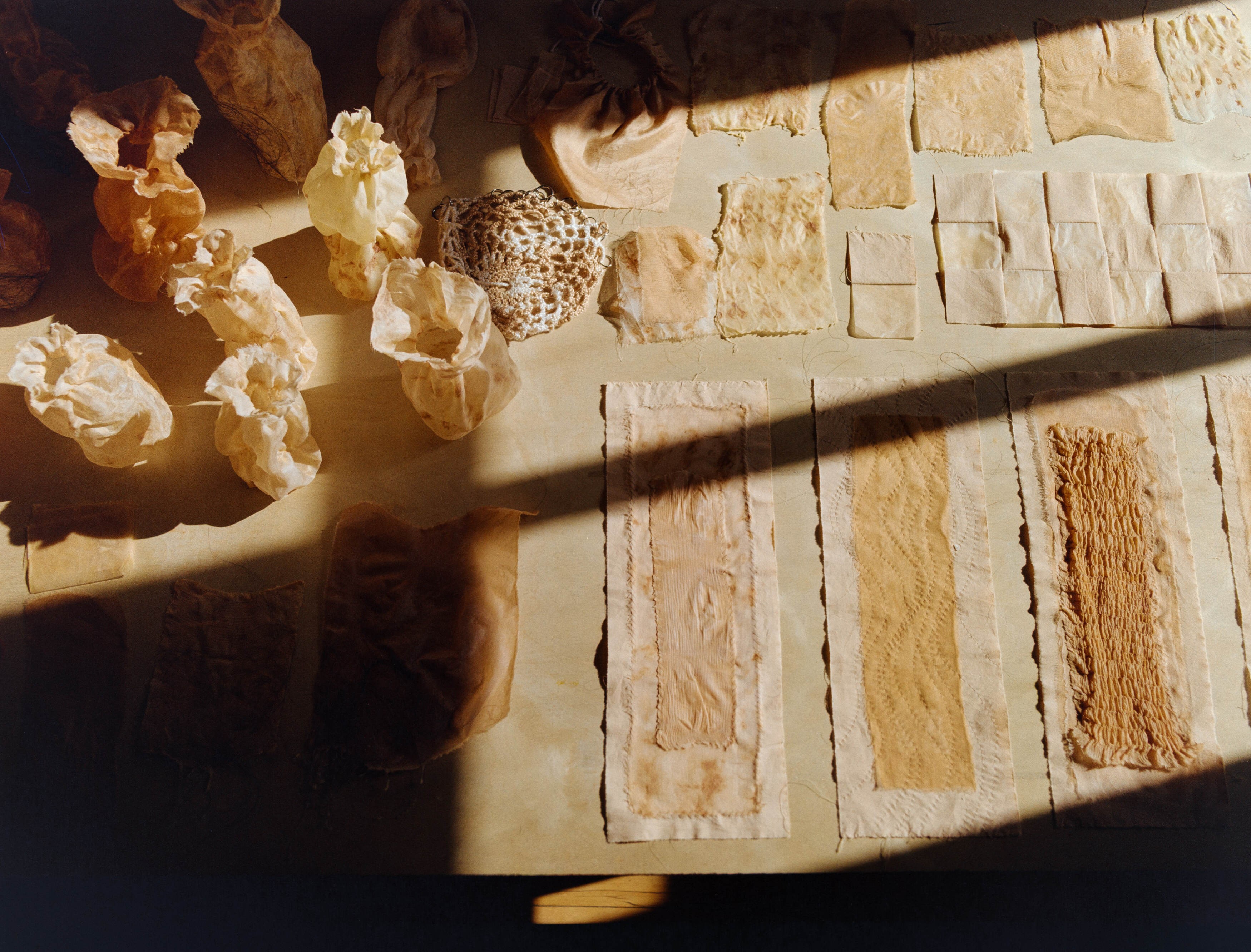 Overhead view of naturally dyed fabric samples and bundles laid out in studio light, Portland artist Laura Kung, medium format film