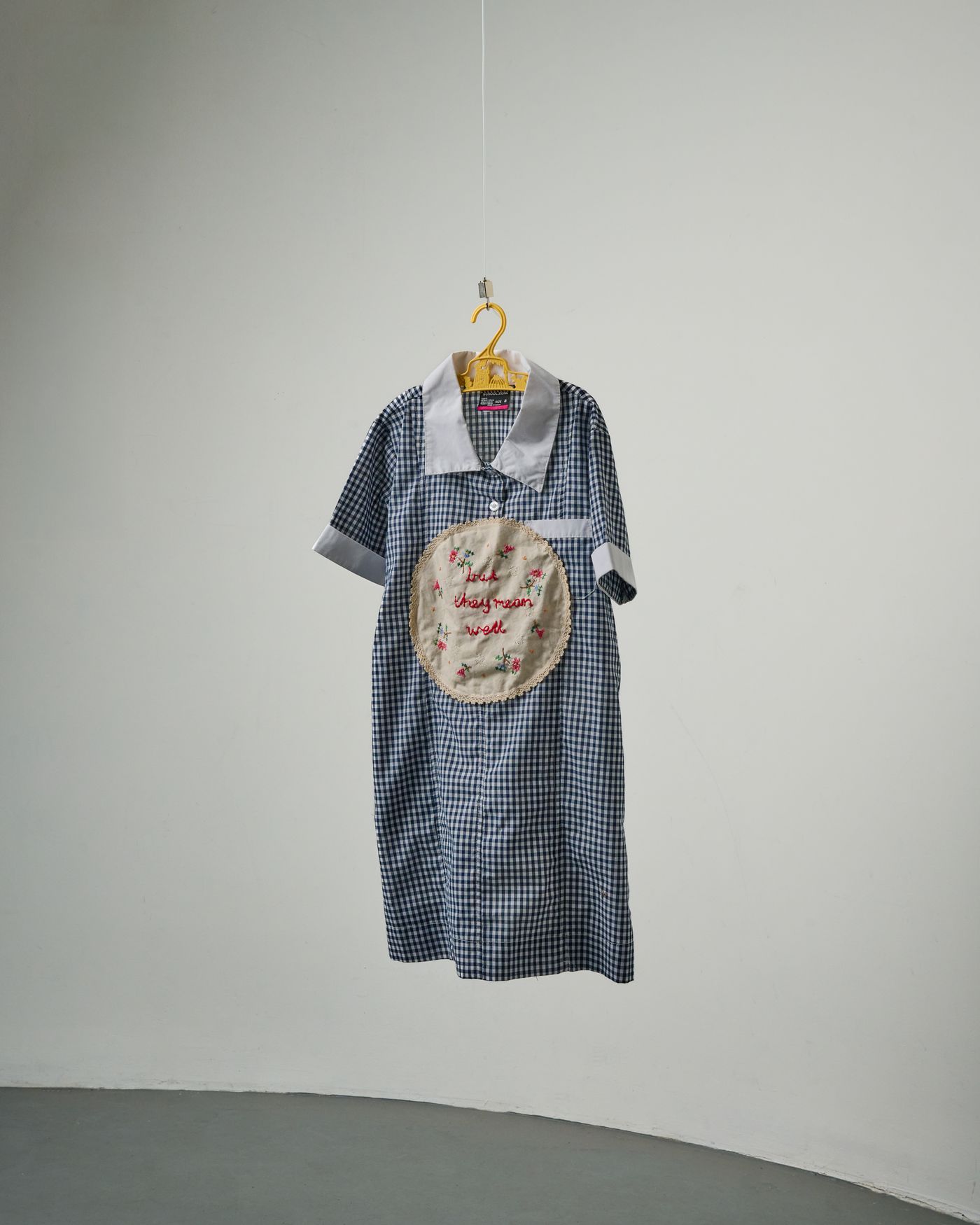 but they mean well — a gingham school dress on a hanger, an embroidered napkin sewn to the front