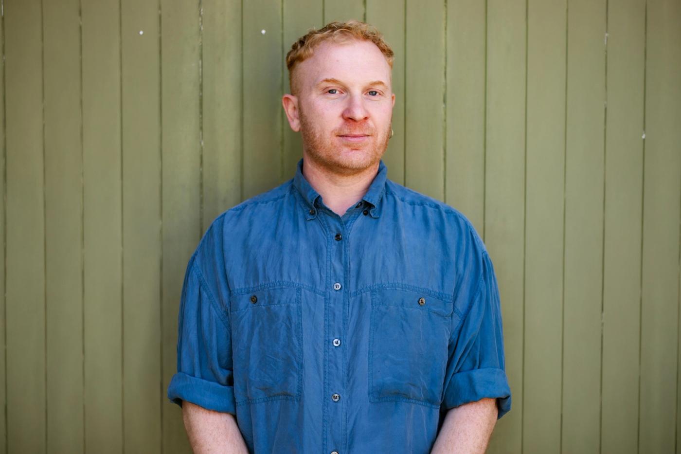 Luke D. King in a blue shirt against a green timber wall. Photo: Emily Short