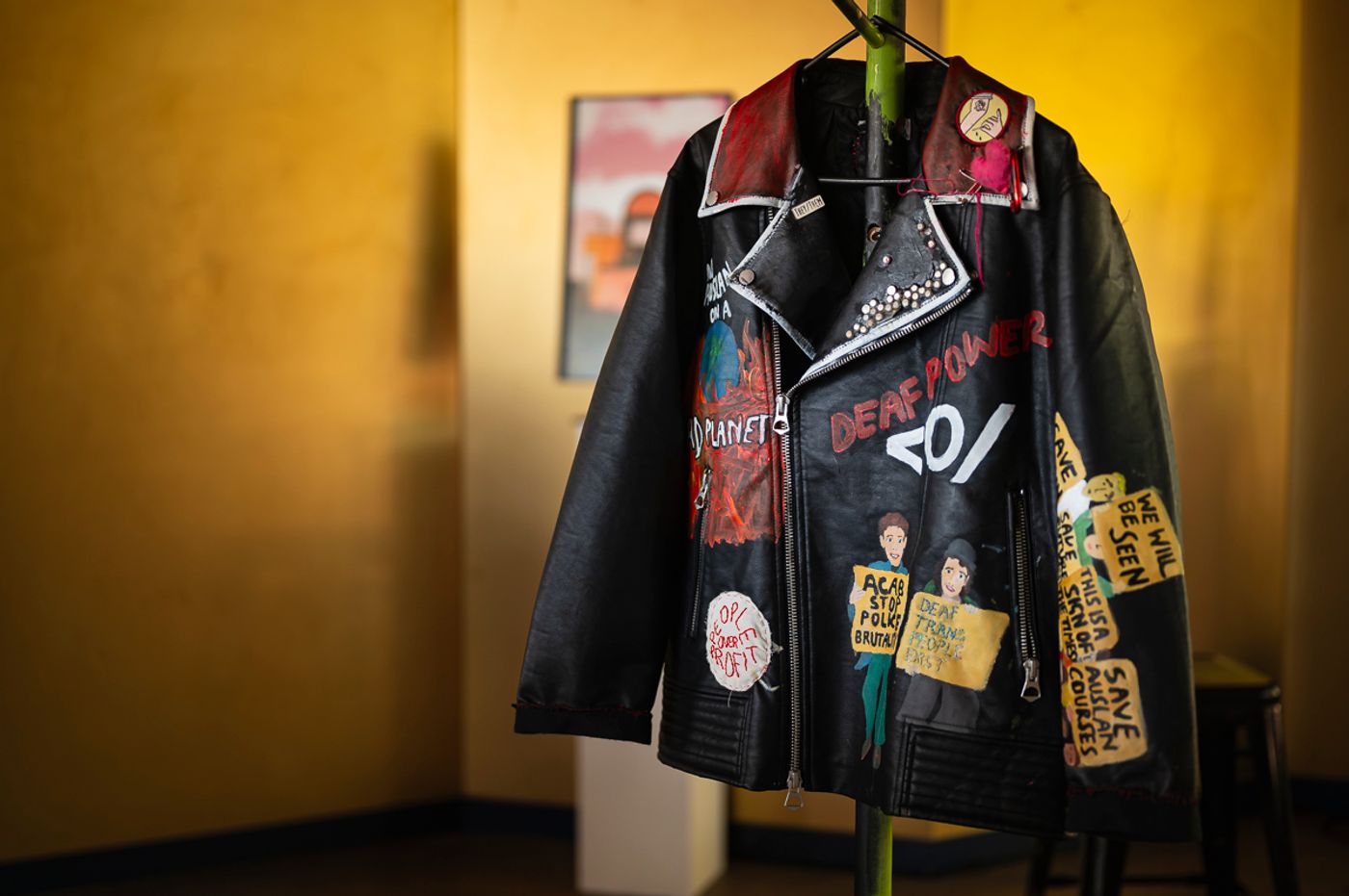 Punk — a black leather jacket hand-painted with Deaf Power and protest slogans, hung on a stand